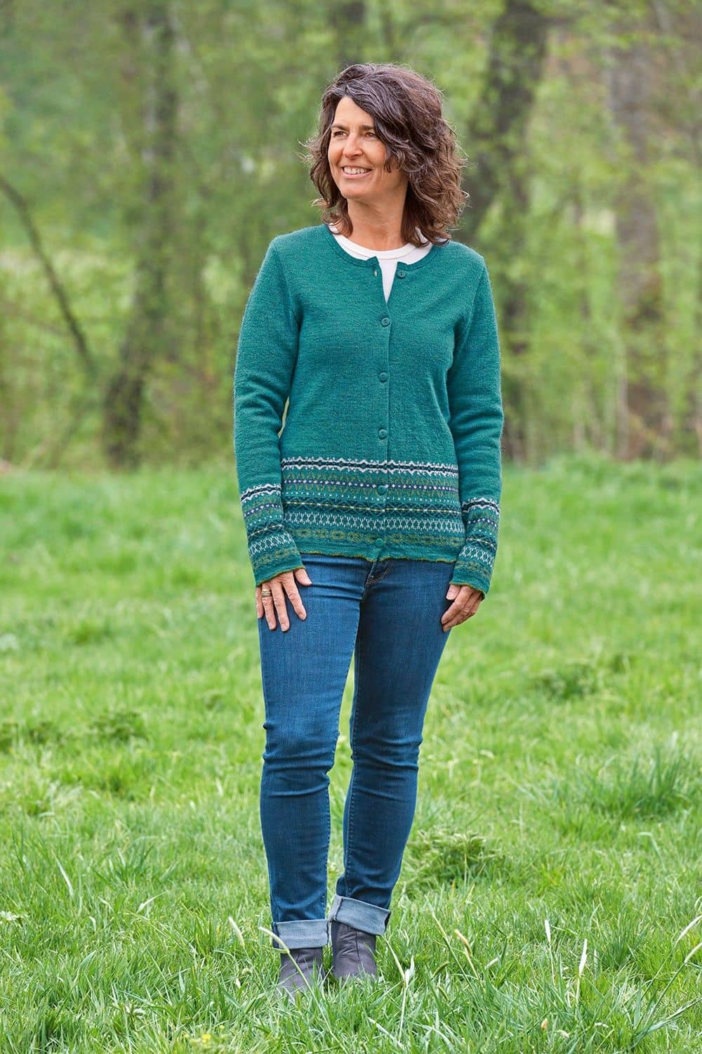 Frau auf Wiese trägt türkise nordic Strickjacke aus bio Wolle (kbT) geschlossen mit einer Jeans