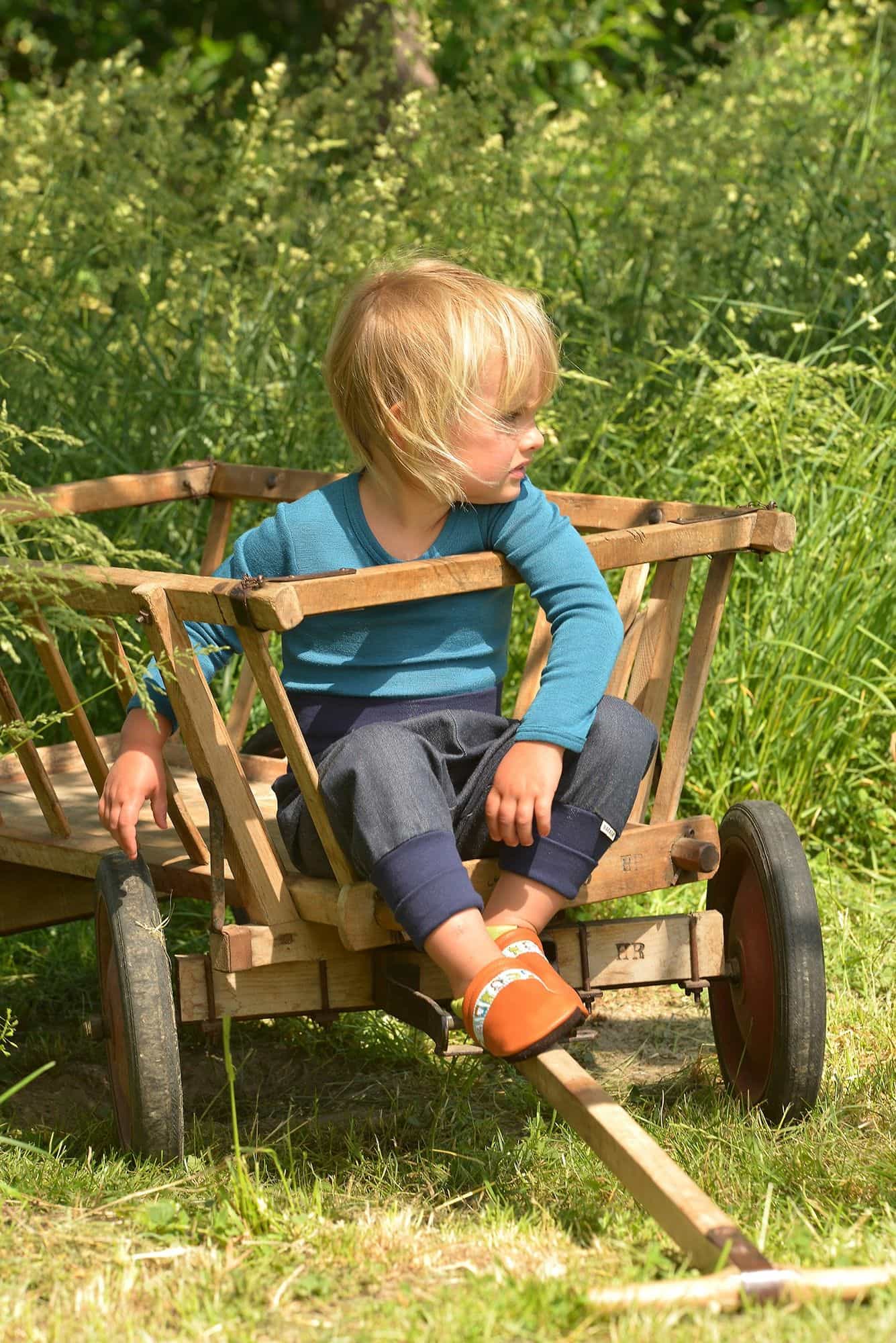 Kind sitzt in Leiterwagen und trägt braune Lederpatschen aus Rindsleder vom Finkhof