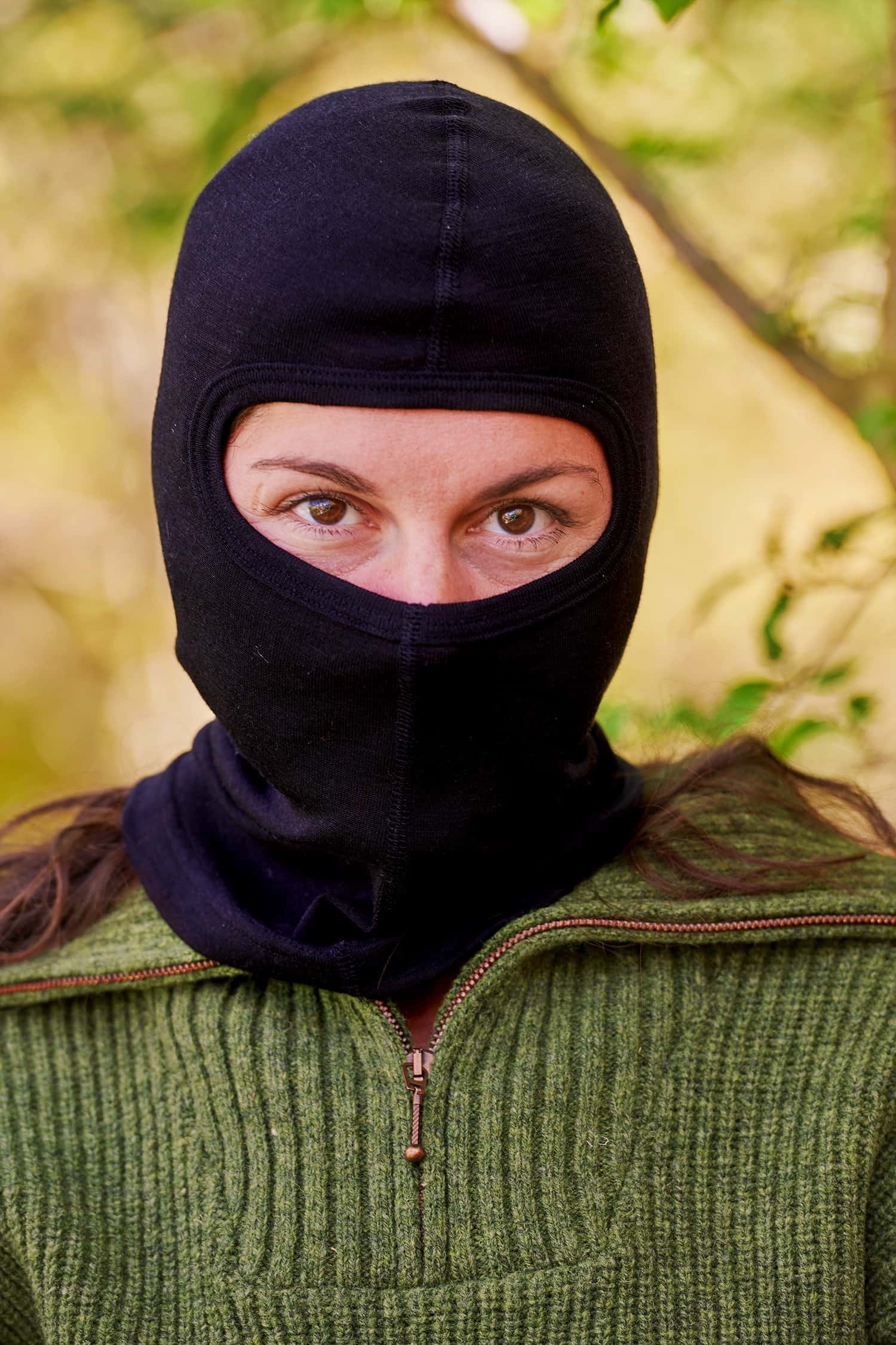 Frau mit grünem Pullover trägt eine schwarze Sturmhaube aus Bio-Wolle und Seide