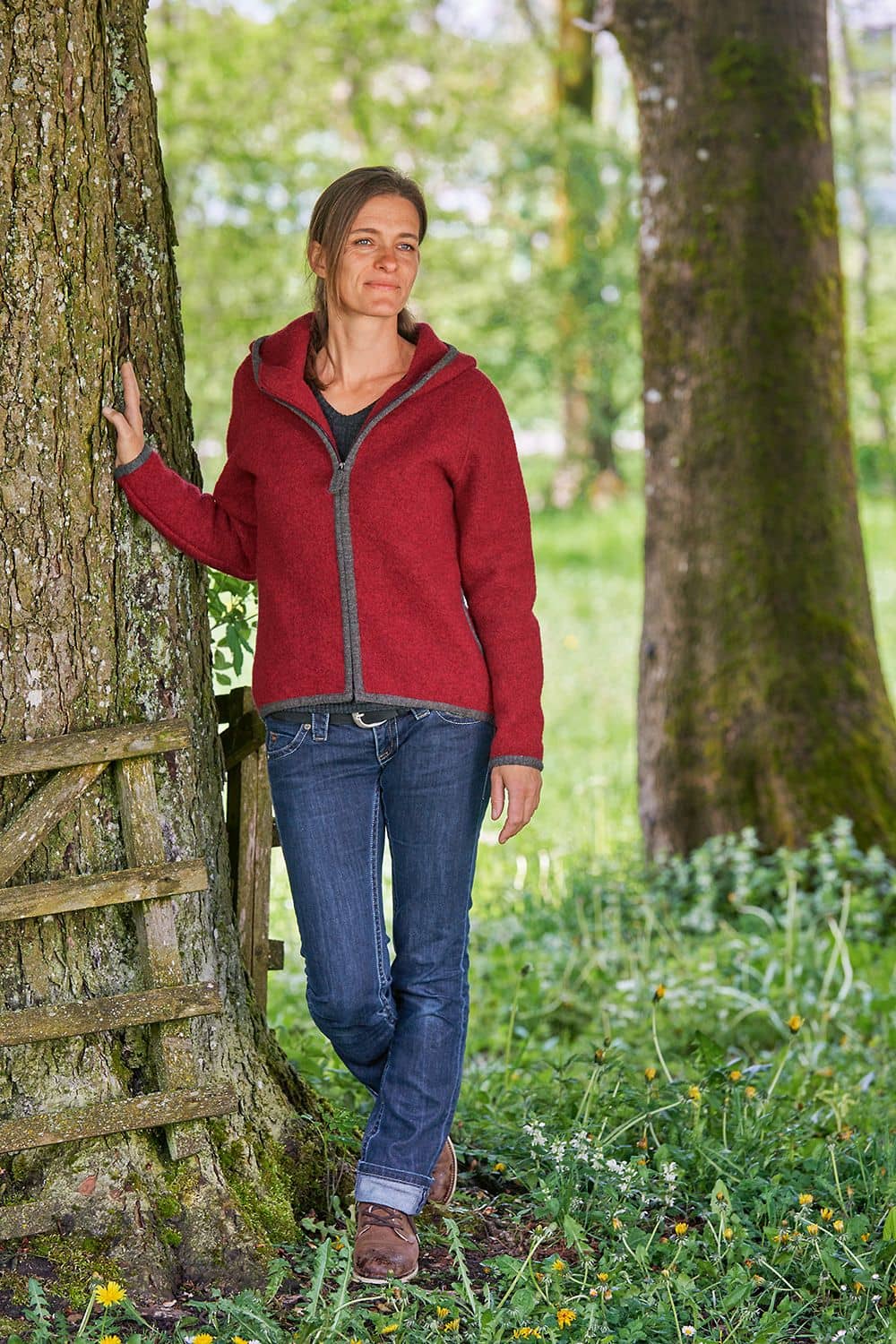 Frau steht neben Baum und trägt rote Jacke aus einem Strickwalk mit bio Wolle (kbT) vom Finkhof