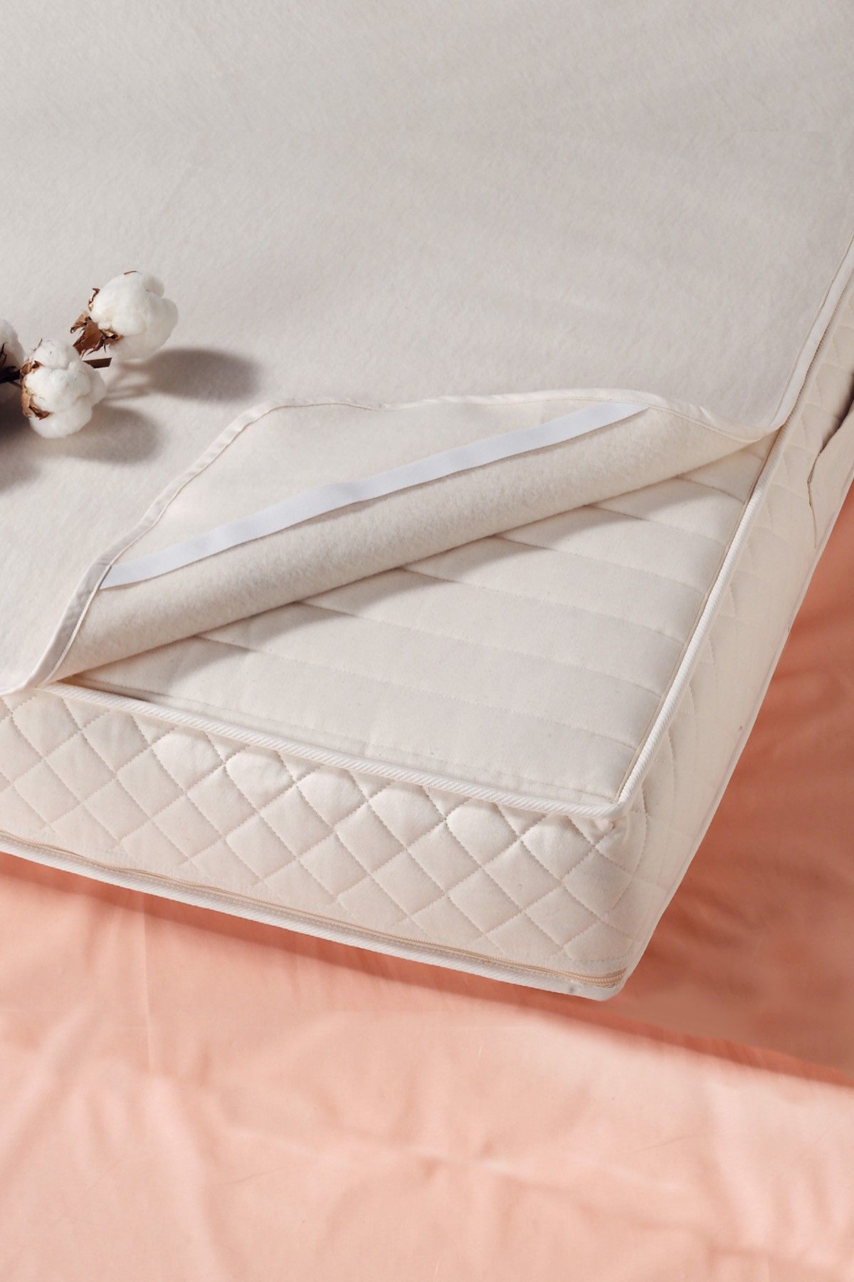 Ecke einer Matratze mit weißer Moltonauflage aus bio Baumwolle (kbA) in 90x200cm, darauf liegt eine Baumwollblüte