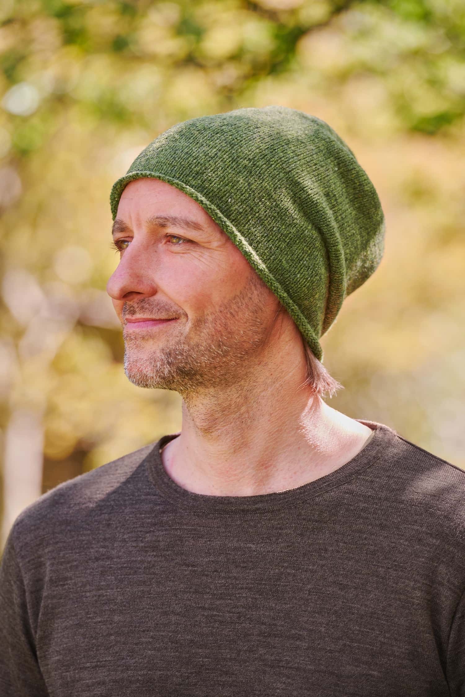 Mann trägt eine grüne Strickmütze mit Rollrand vom Finkhof aus Bio-Wolle und ein braunes Shirt