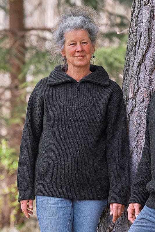 Frau mit Jeans steht neben Baum und trägt anthraziten Finkhof Troyer mit Zipper aus bio Wolle (kbT)