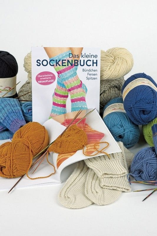 Das kleine Sockenbuch Das kleine Sockenbuch zwischen Wollknäulen in verschiedenen Farben und Nadeln
