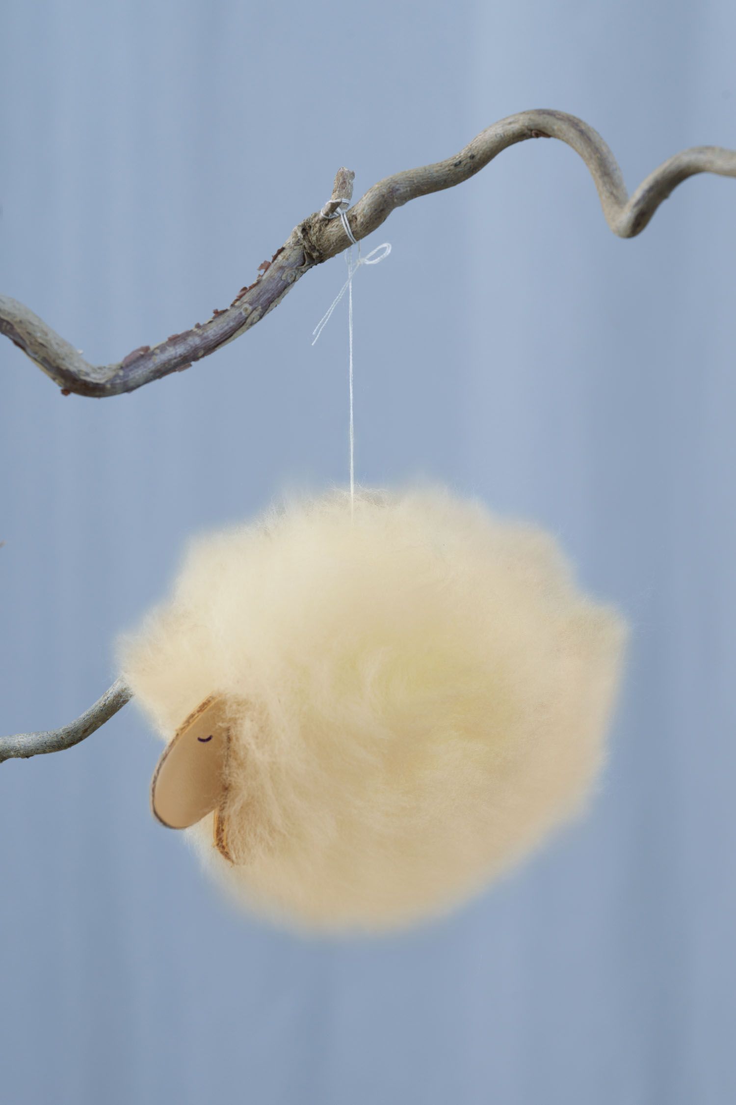 einzelnes weißes Schäfchen aus der Finkhof Bastelapackung für ein Mobile aus Schaffell und Leder hängt an einem Ast