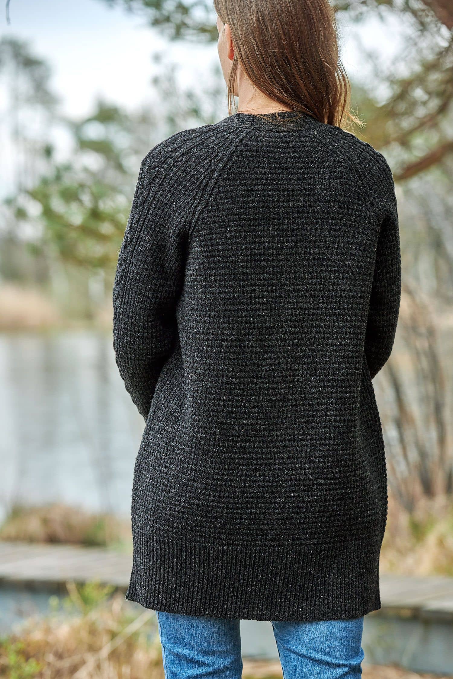 Frau die anthrazitfarbenen Cardigan vom Finkhof mit Zopfmuster aus bio Wolle (kbT) trägt, von hinten fotografiert