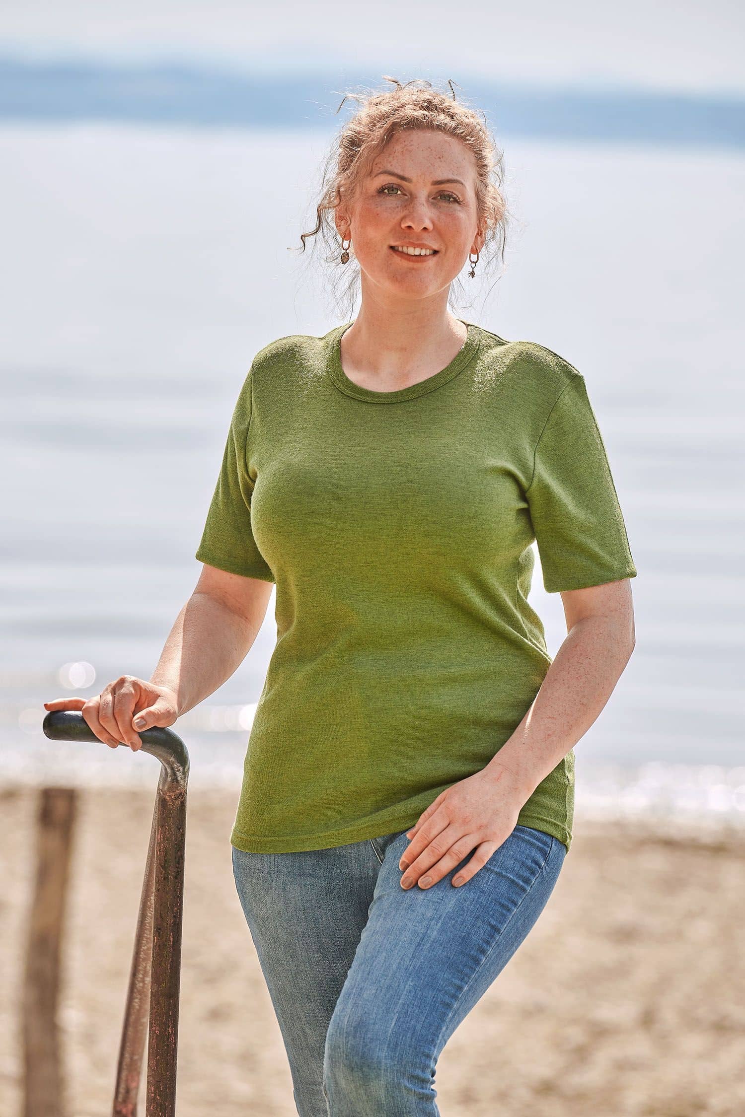 Frau trägt eine Jeans und ein grünes kurzärmeliges Wollhemd aus bio Merinowolle (kbT)