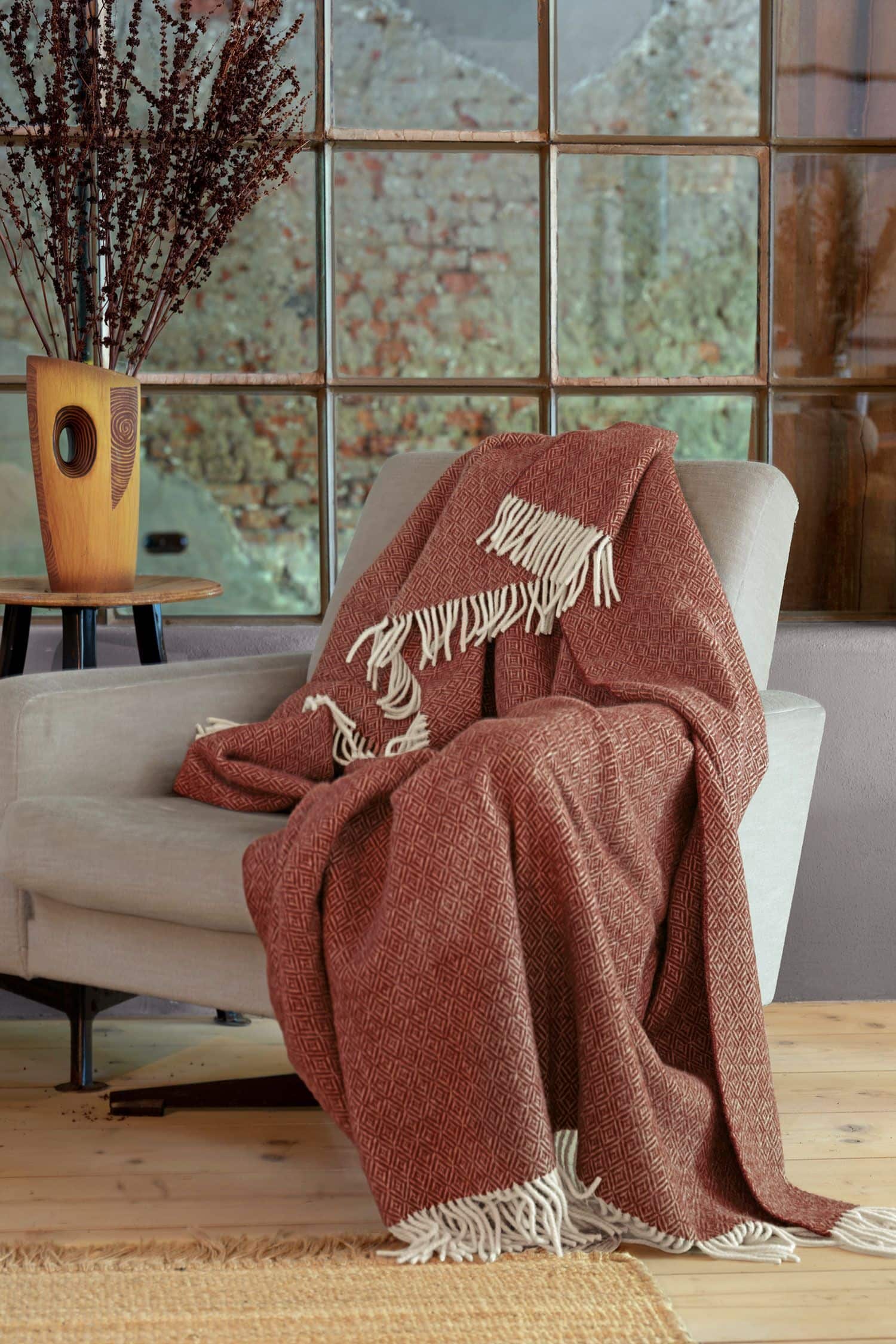 Finkhof-Plaid aus regionaler Bio-Schurwolle altrosafarbenes Finkhof Plaid Siena aus bio Wolle (kbT) liegt auf beigem Sessel