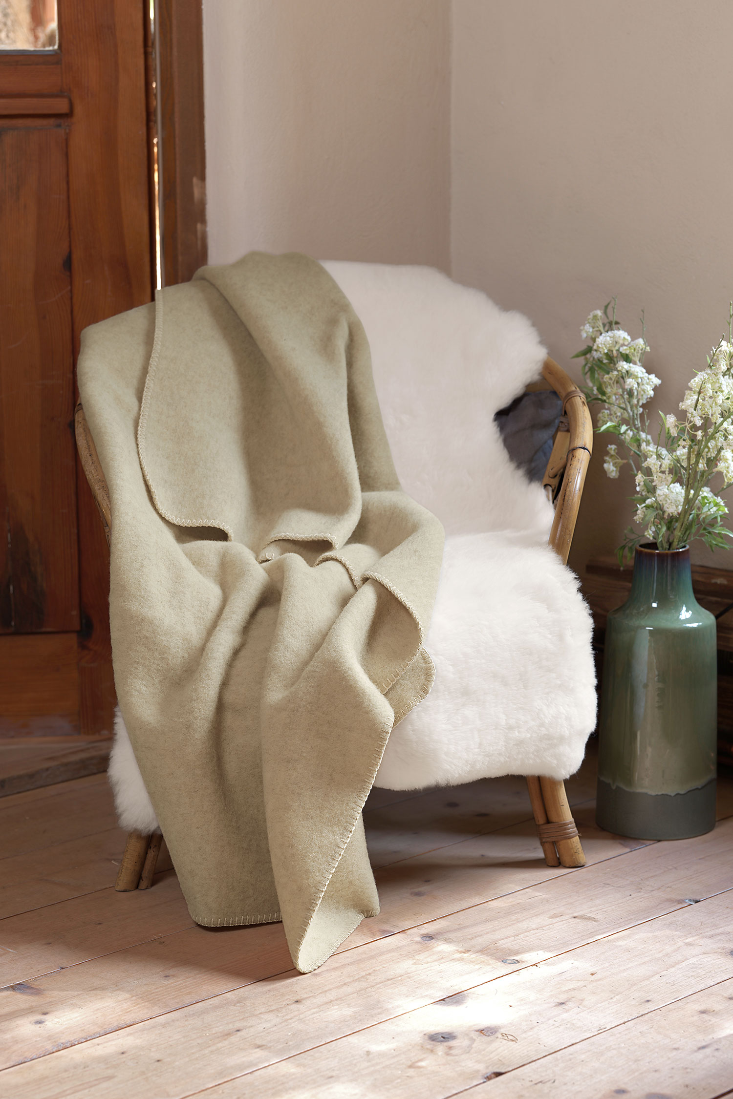 beige Wolldecke aus bio Wolle (kbT) vom Coburger Fuchsschaf vom Finkhof liegt auf Korbstuhl mit weißem Fell
