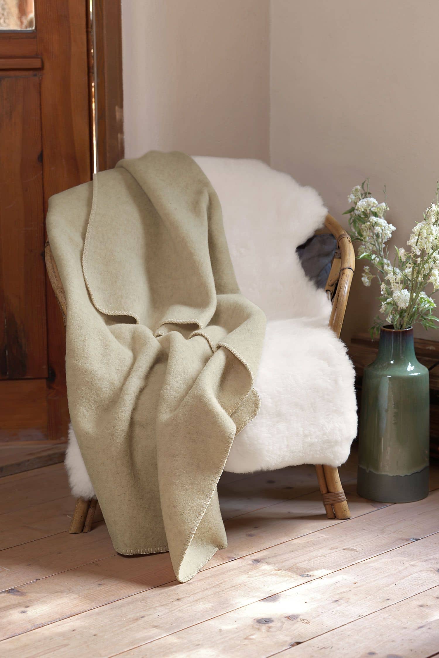 beige Wolldecke aus bio Wolle (kbT) vom Coburger Fuchsschaf vom Finkhof liegt auf Korbstuhl mit weißem Fell