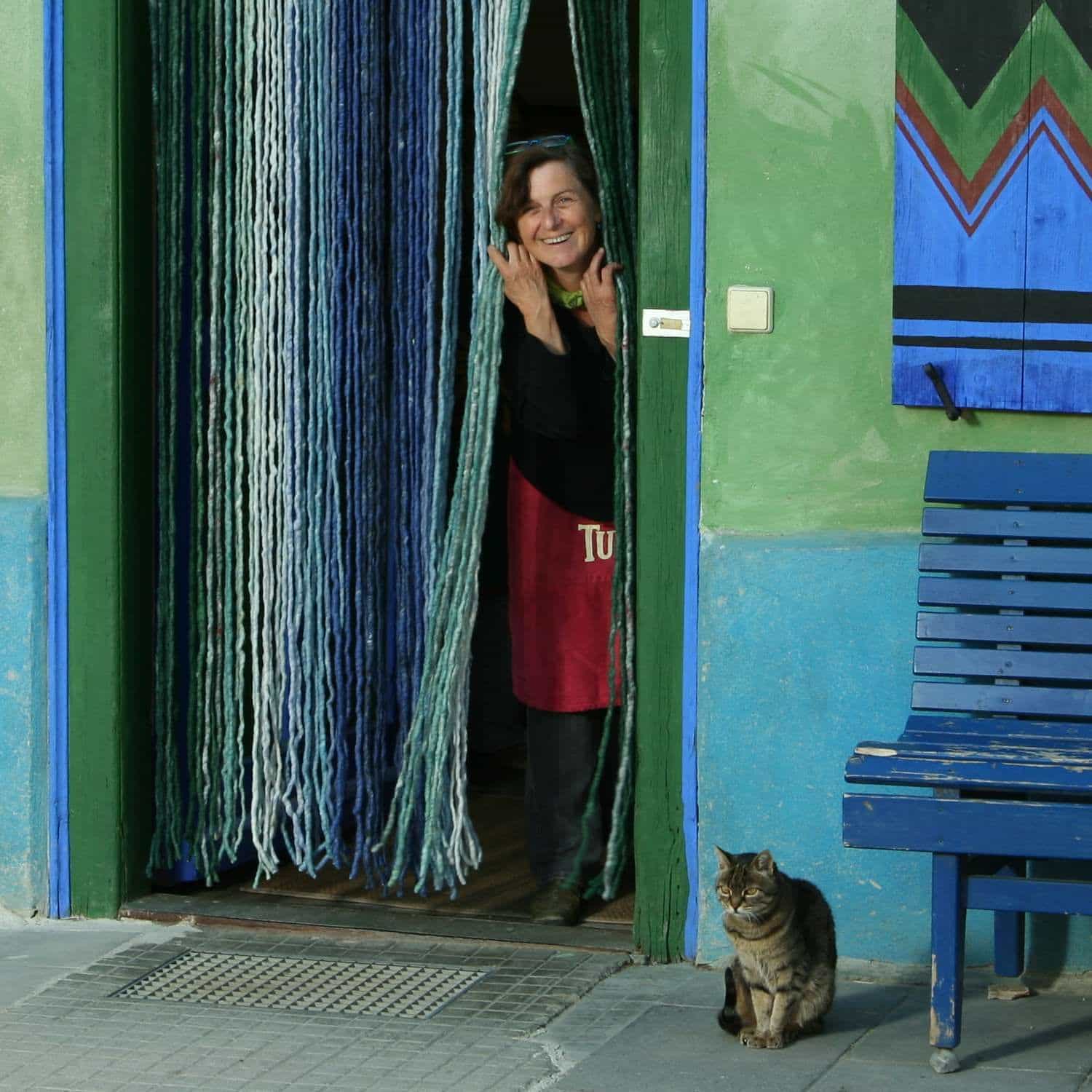 Frau schaut durch blauen Türvorhang von grün blauem Haus