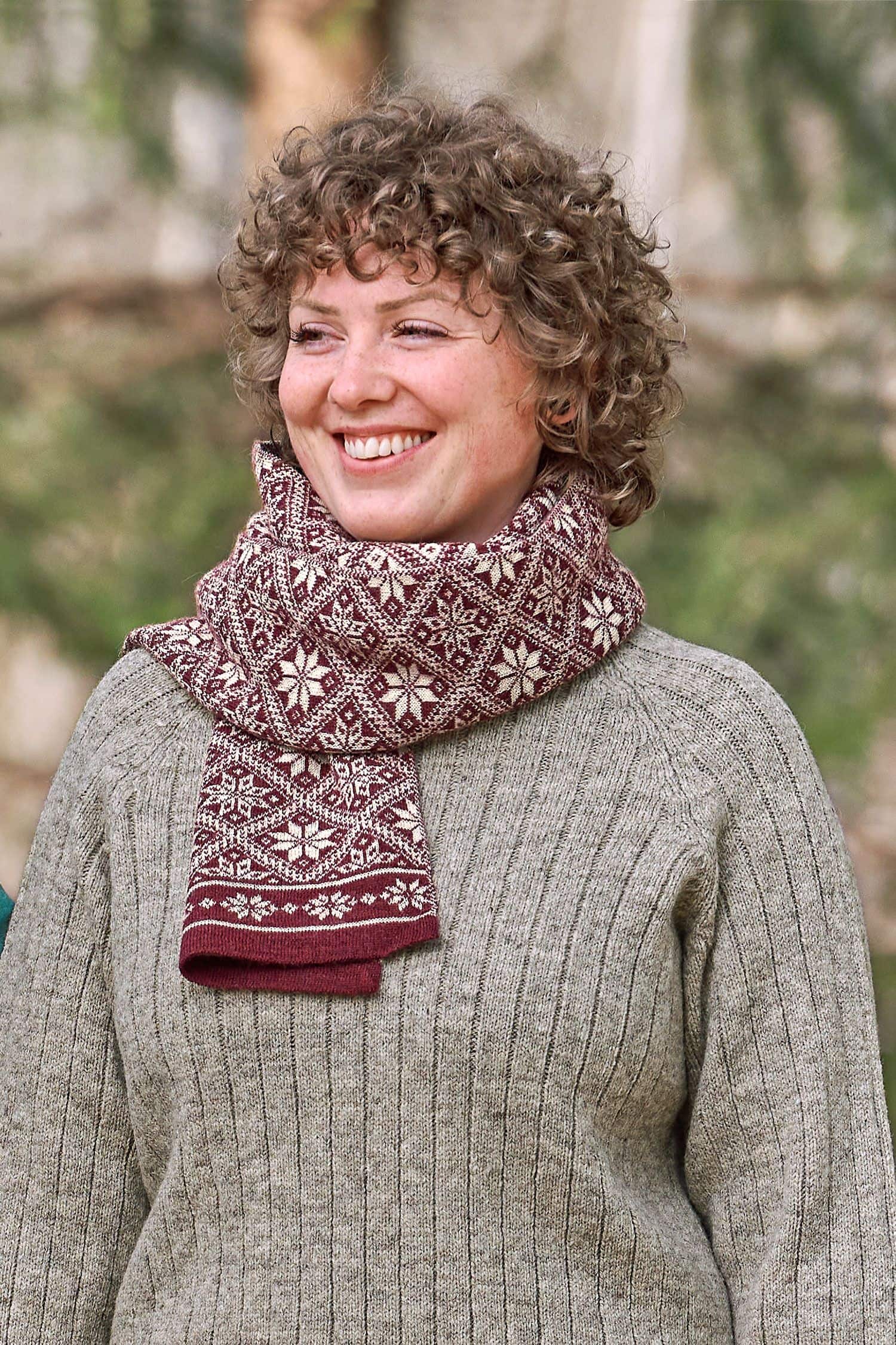 Frau trägt braunen Pulli und roten Schal aus bio Wolle (kbT) mit winterlichem Muster