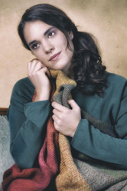 Frau mit blauem Pullover schmiegt sich an Finkhof Regenbogen Wolldecke aus bio Wolle (kbT)