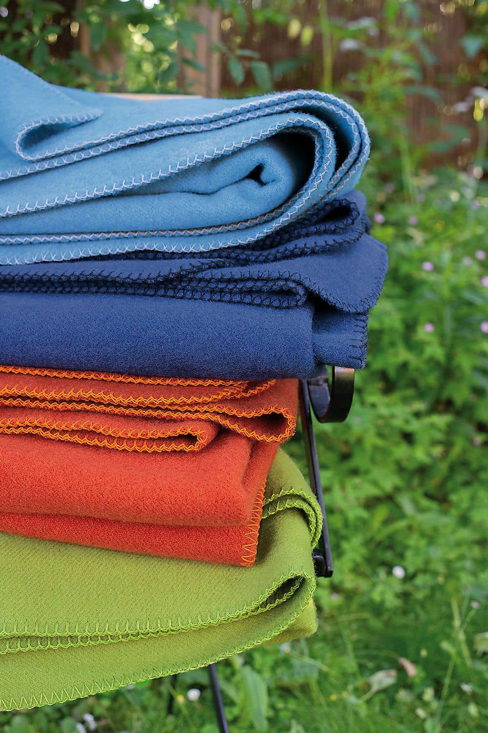 Wolldecke Malin Wolldecken aus bio Wolle (kbT) vom Finkhof für Kinder in dunkelblau, rot und grün gestapelt mit natürlichem Hintergrund