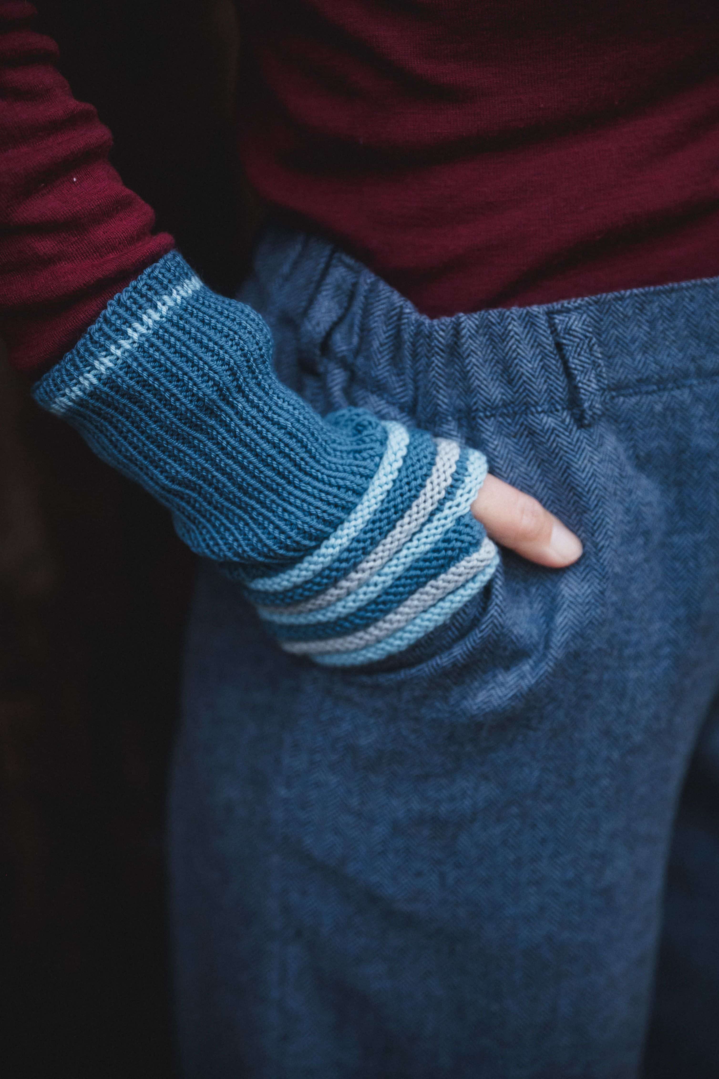 Hände mit blauen Stulpen in Taschen einer blauen Stoffhose und rotes Shirt
