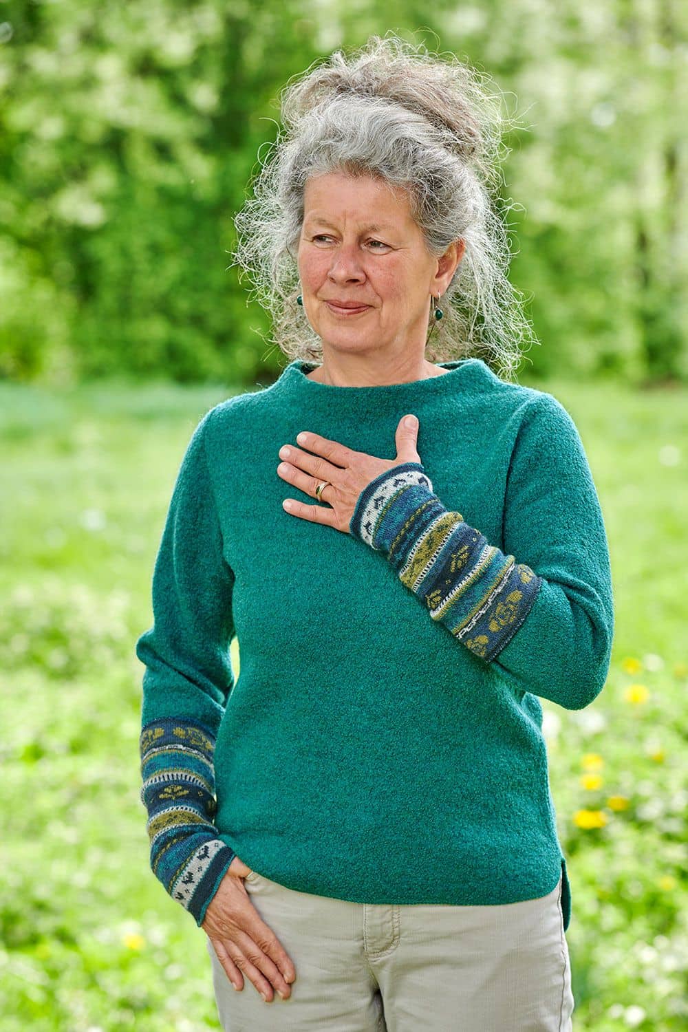Frau mit türkisem Pullover trägt blau grüne gemusterte Armstulpen aus bio Wolle (kbT)