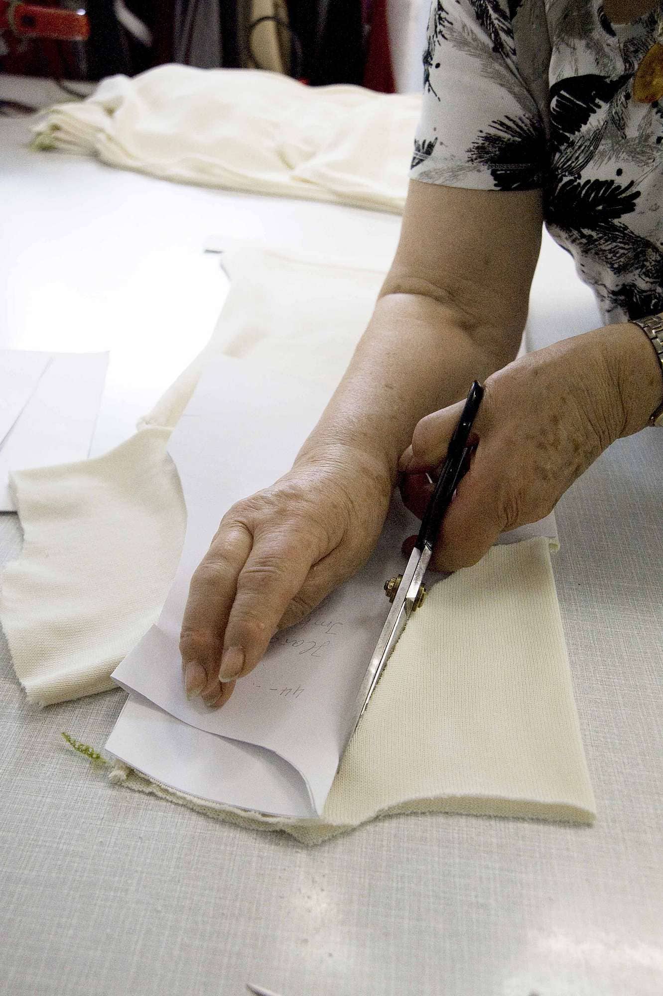 ueber-uns-unsere-wolle-strickerei-web-067 Frau schneidet mithilfe von Schnittmuster weißen Finkhof Stoff zu