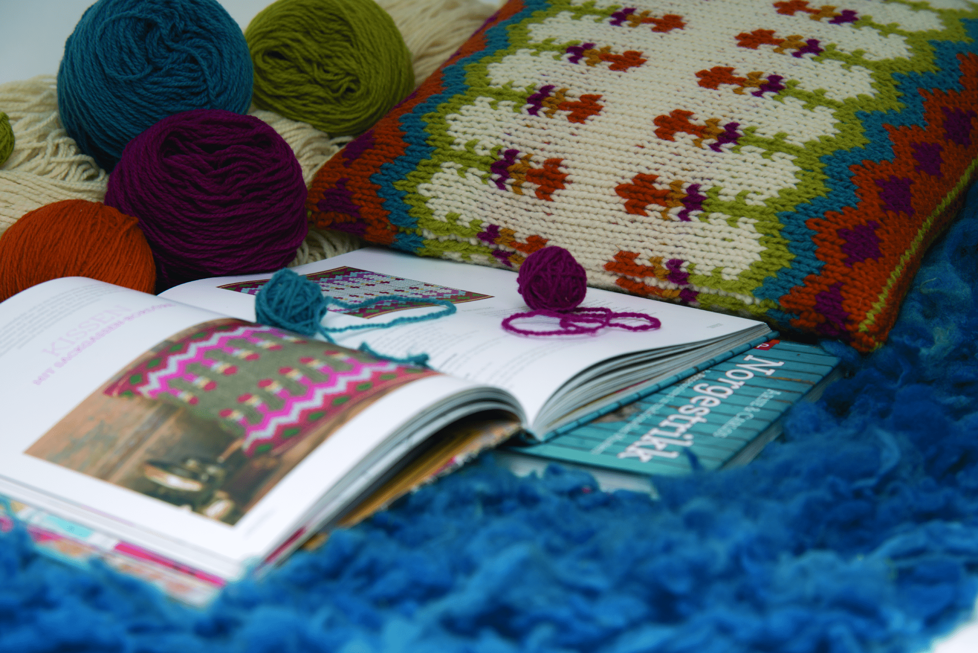 Buch mit Strickanleitungen auf einer Decke mit Wollknäulen