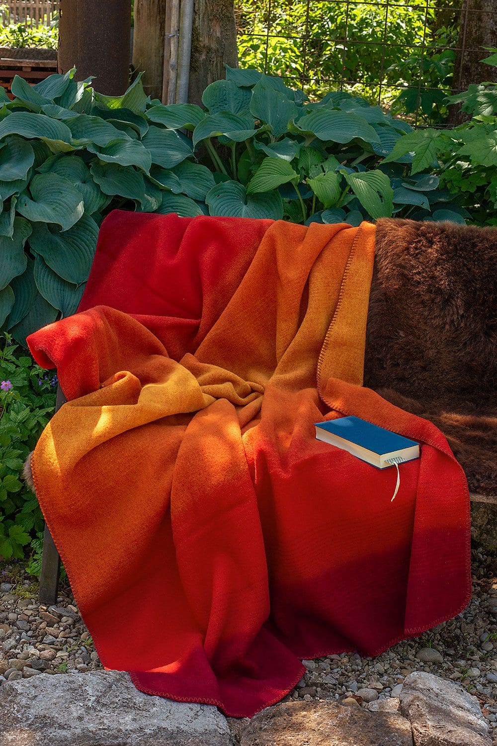Wolldecke Herbst (kbT) 150 x 200 cm rot orange Wolldecke aus bio Wolle (kbT) liegt auf Bank mit Pflanzen im Hintergrund