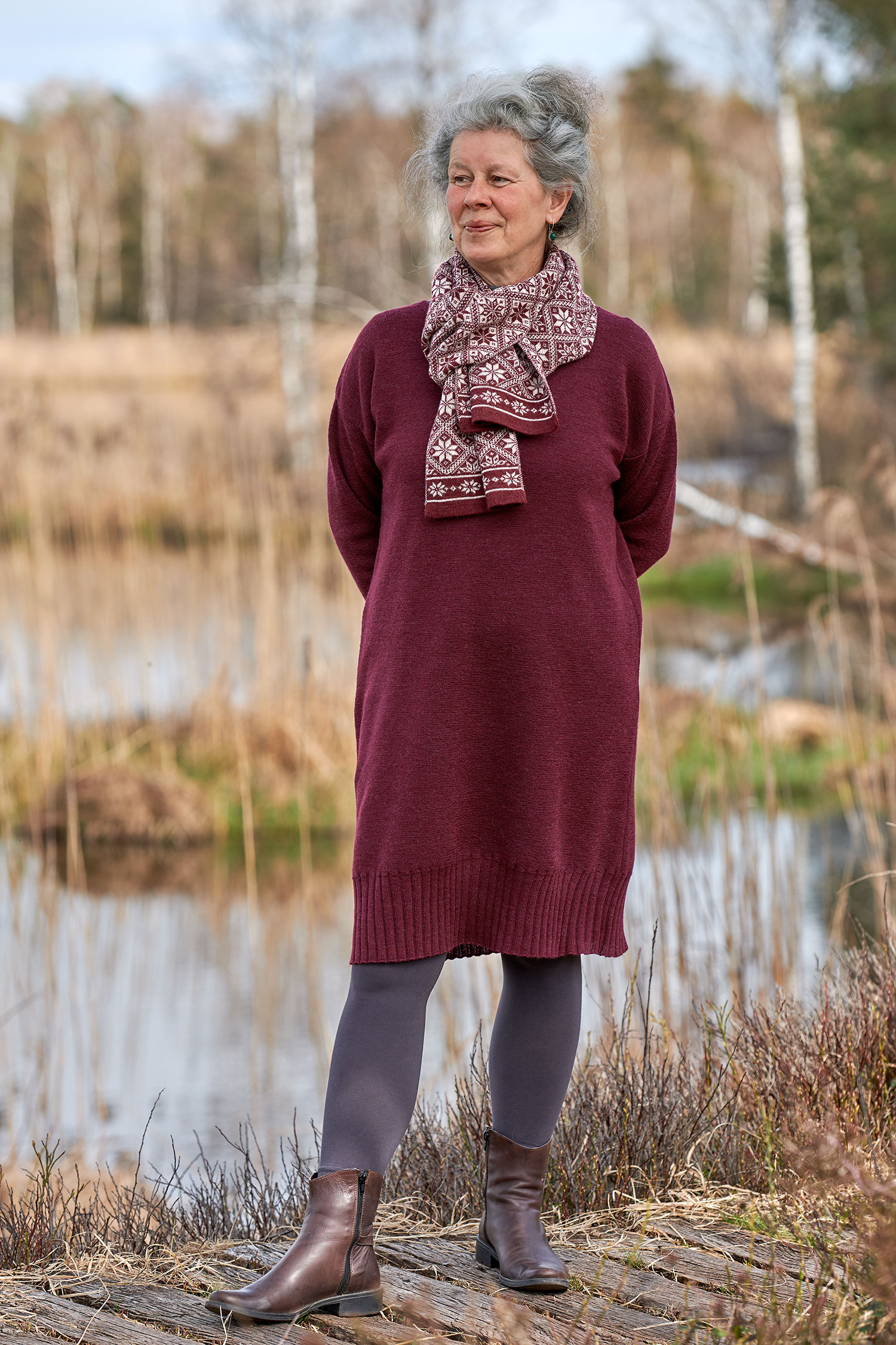 Frau trägt burgunderrotes Strickkleid aus bio Wolle (kbT), dazu einen rot gemusterten Schal