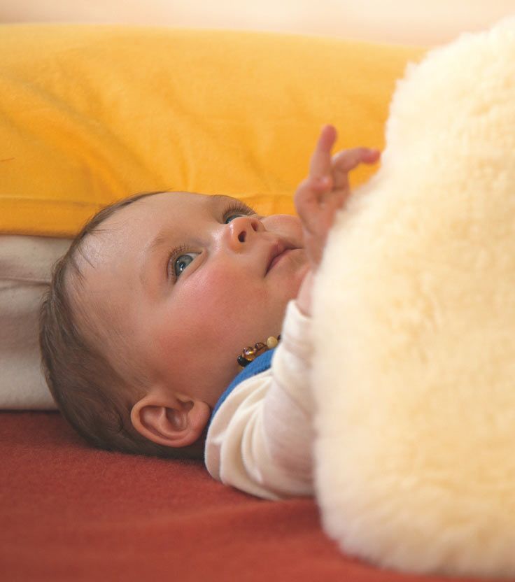 Baby liegt auf rotem Laken mit gelbem Kissen und ist mit einem Finkhof Fell zugedeckt
