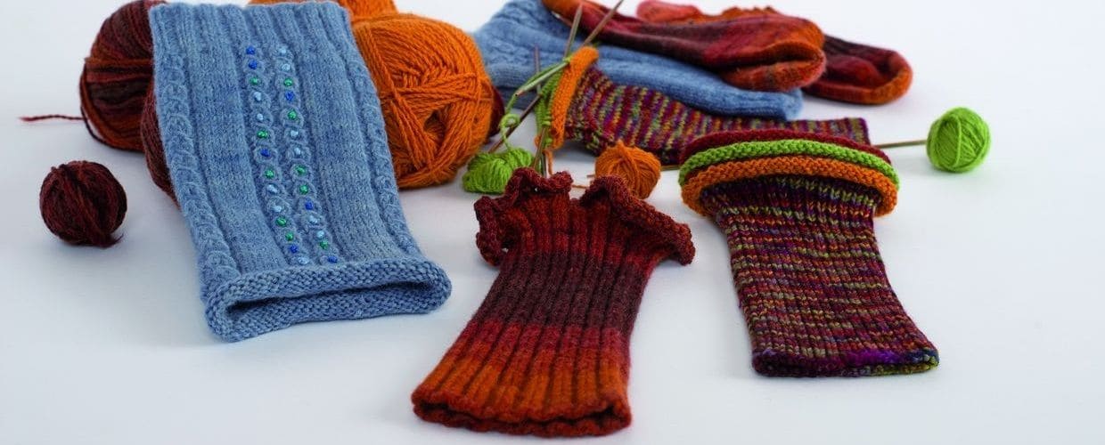 bunte Stulpen und Wollknäule liegen auf weißem Untergrund