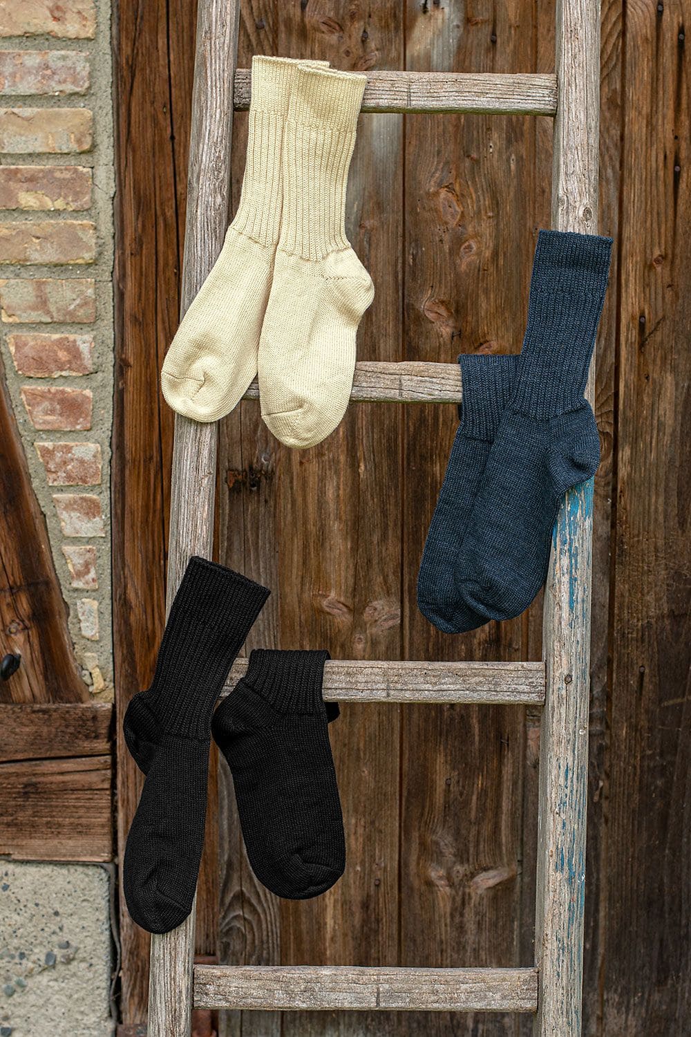 Mittlere Wollsocken mittlere Wollsocken aus bio Wolle (kbT) in allen drei Farben als Paare über Holzleiter gehängt vor Holzwand