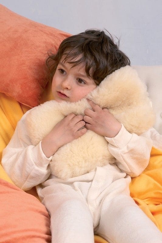 Kind mit Schlafanzug kuschelt sich an relugan gegerbtes Finkhof Schaffell mit gelblichem Unterton