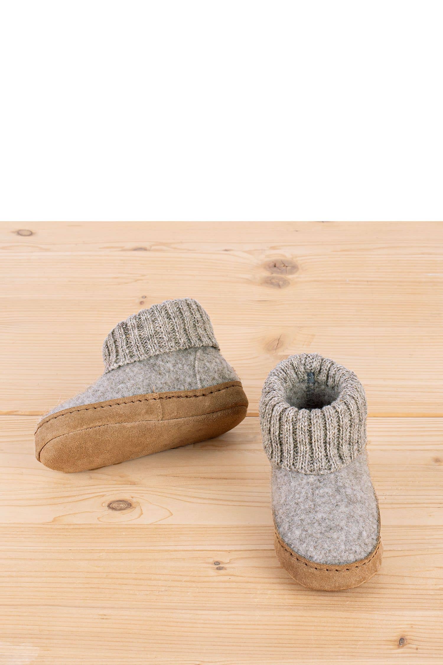 hellgraue Kinderhüttenschuhe vom Finkhof aus bio Wolle (kbT) und pflanzlich gegerbtem Leder stehen auf Holzboden