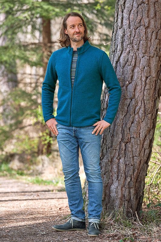 Jacke Jon Mann steht vor Baum und trägt Ringelshirt, türkise Jacke aus bio Wolle (kbT) mit Stehkragen und Jeans