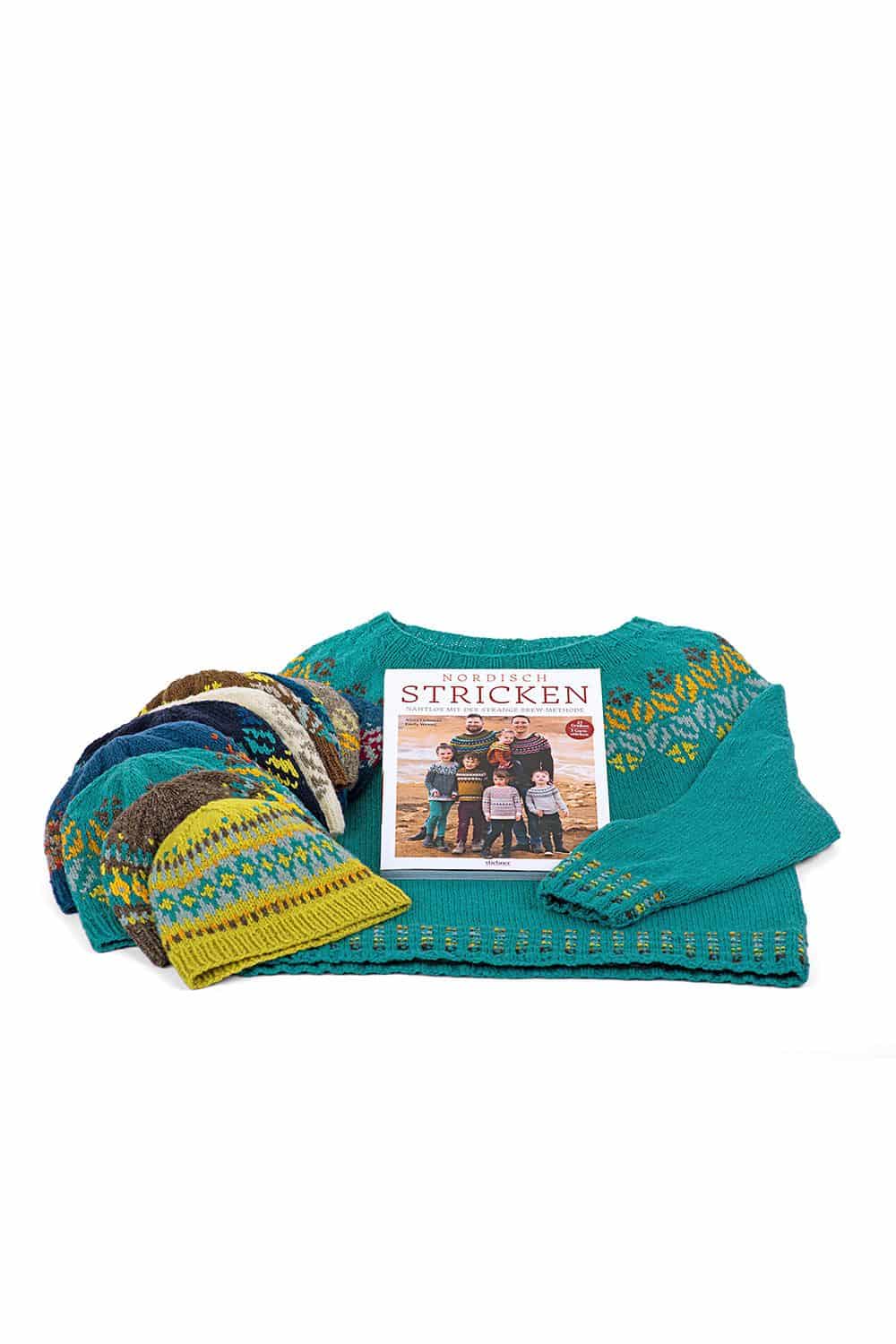 Nordisch Stricken auf türkisem Pulli liegen Mützen mit Muster und das Buch ,,Nordisch stricken"