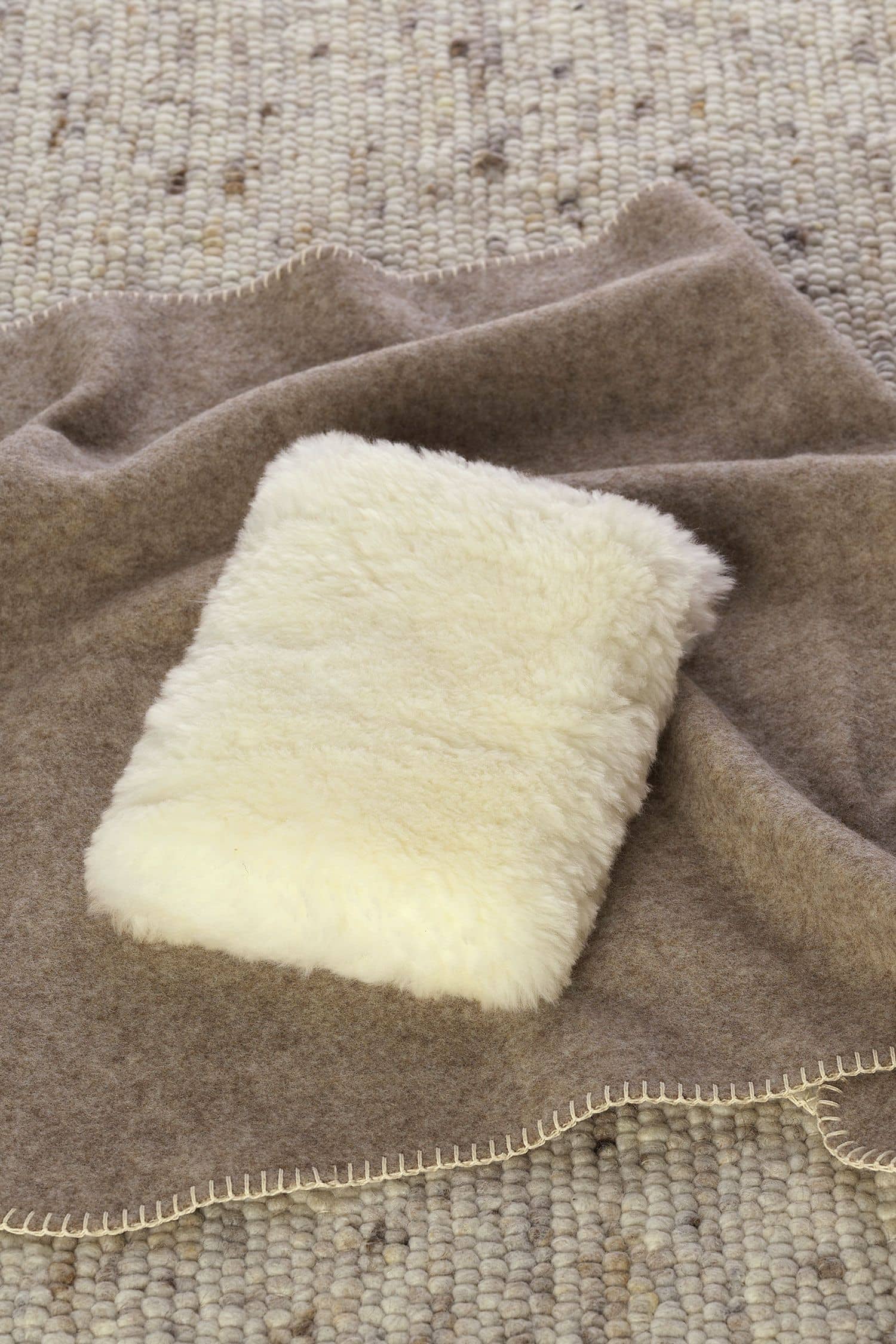 quadratisches weißes Kuschelkissen aus pflanzlich gegerbtem Schaffell vom Finkhof auf einer braunen Decke