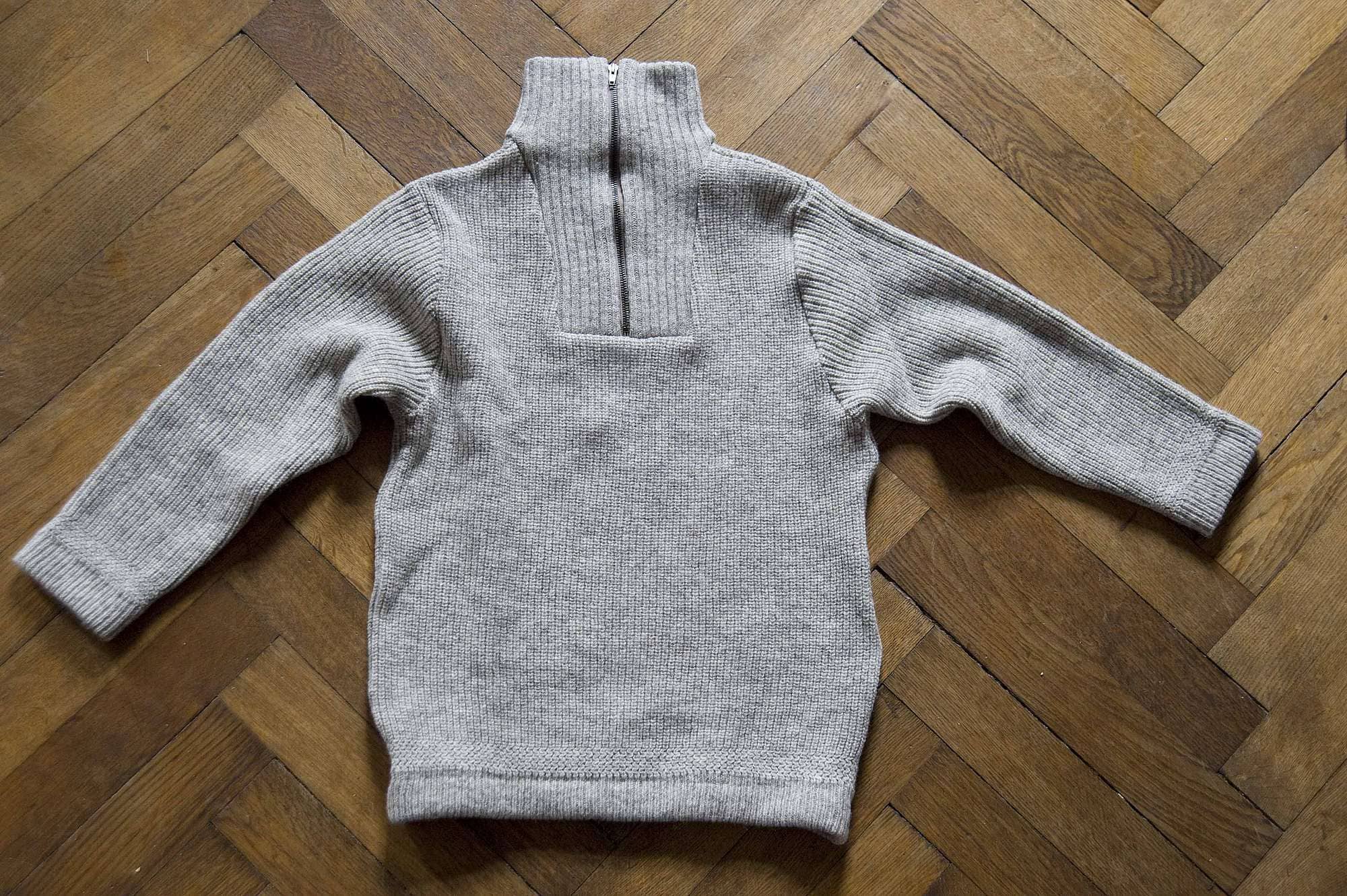 ueber-uns-unsere-wolle-finkhof-pullover-web_1 hellbrauner Finkhof Pullover mit Zipper liegt auf braunem Holzboden