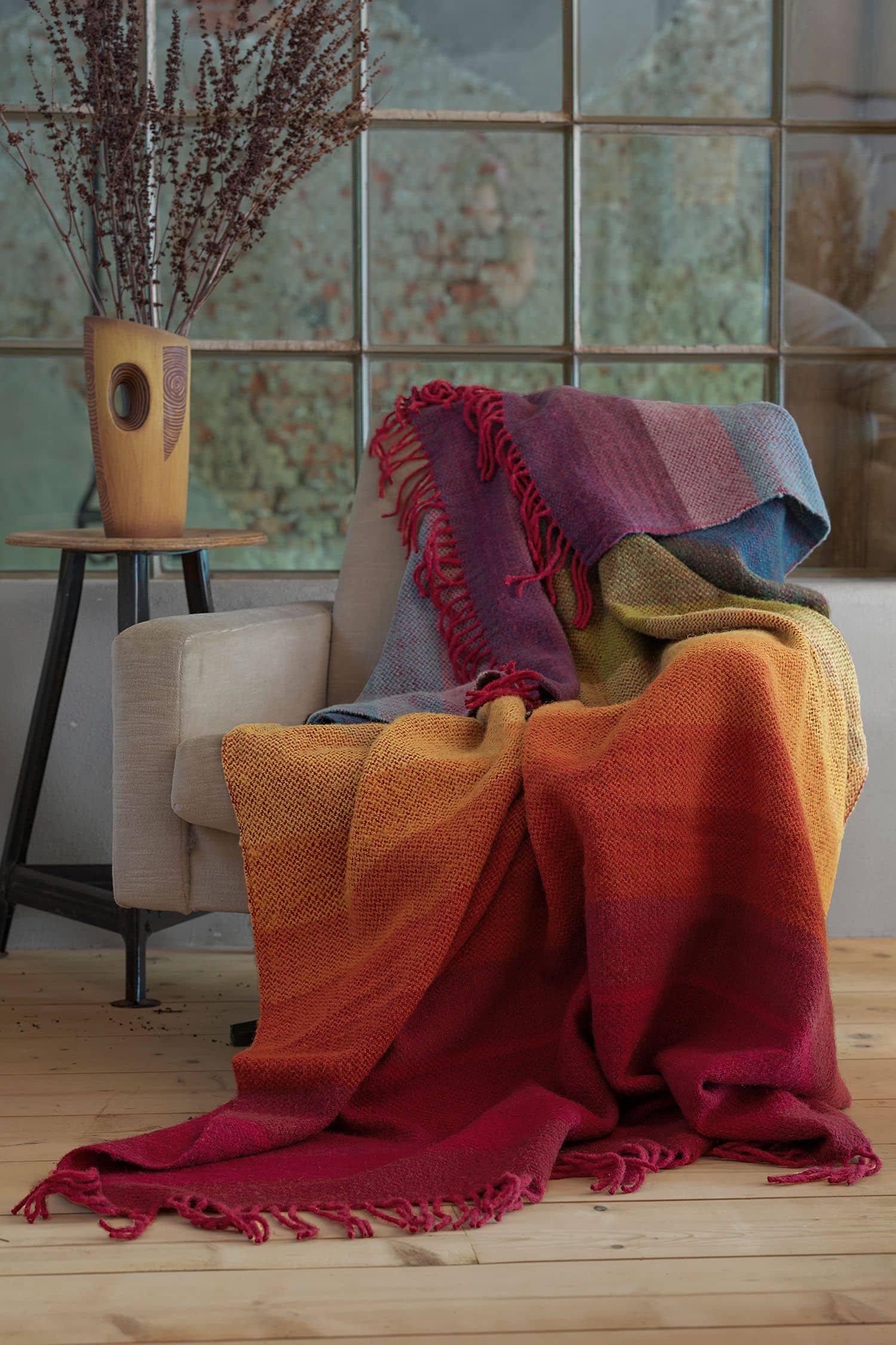 Wolldecke Regenbogen 150 x 200 cm regenbogenfarbene Wolldecke aus bio Wolle (kbT) vom FInkhof liegt auf hellgrauem Sessel