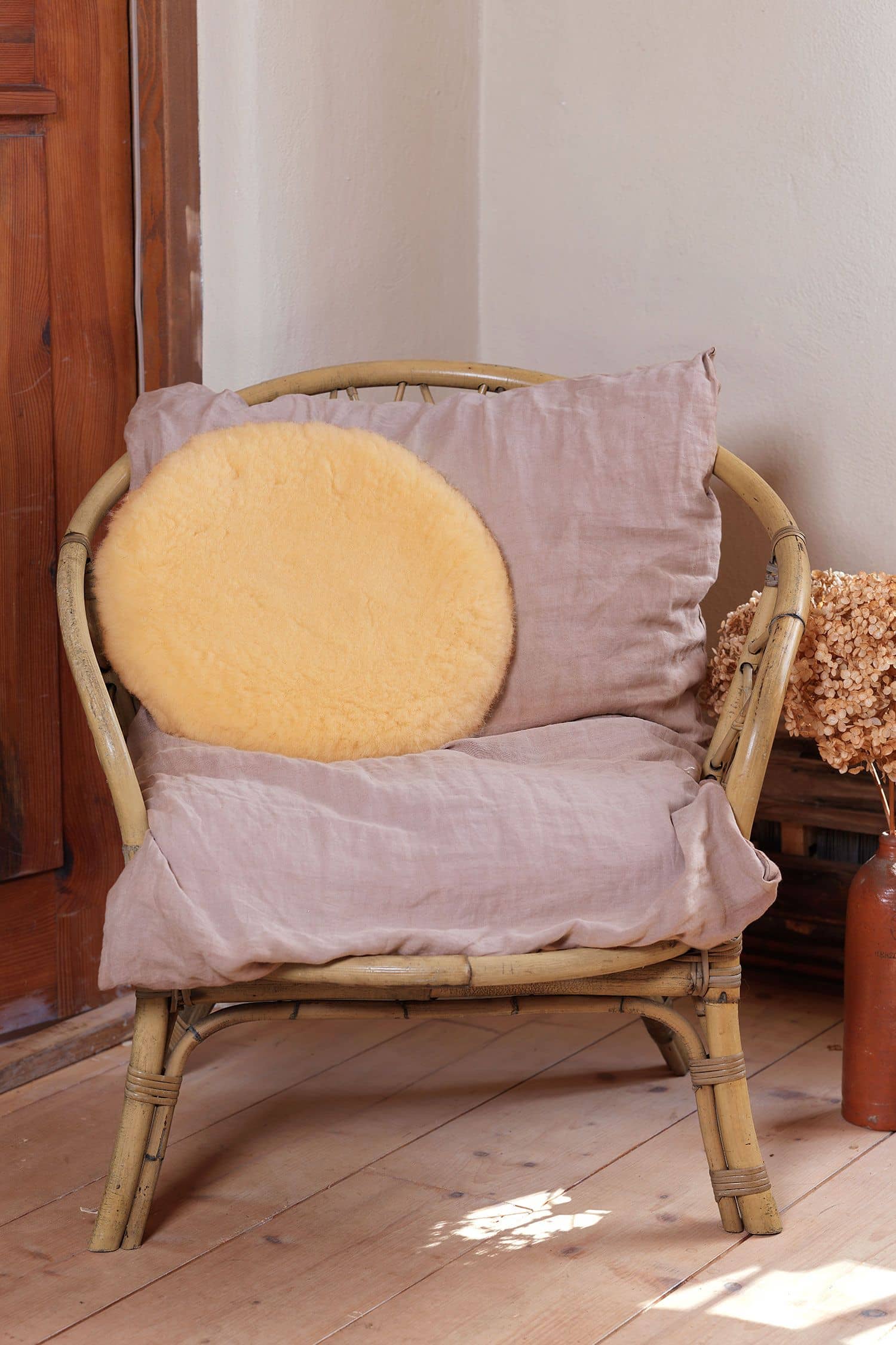 rundes Wohlfühlkissen aus relugan gegerbtem Finkhof Fell liegt auf einem Korbstuhl