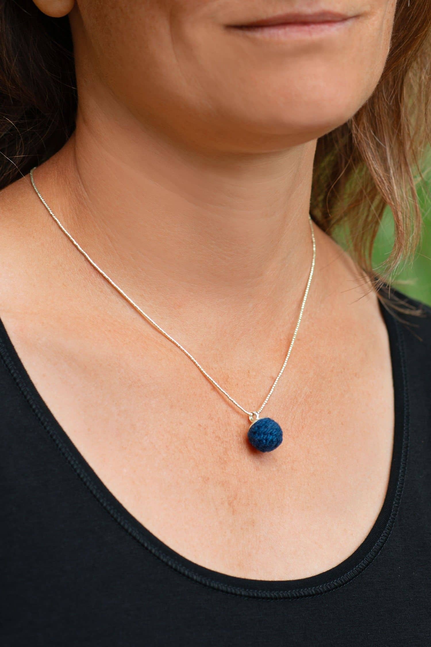 Frau mit schwarzem Shirt trägt blaue handgemachte Wollperle aus pflanzengefärbter Schurwolle