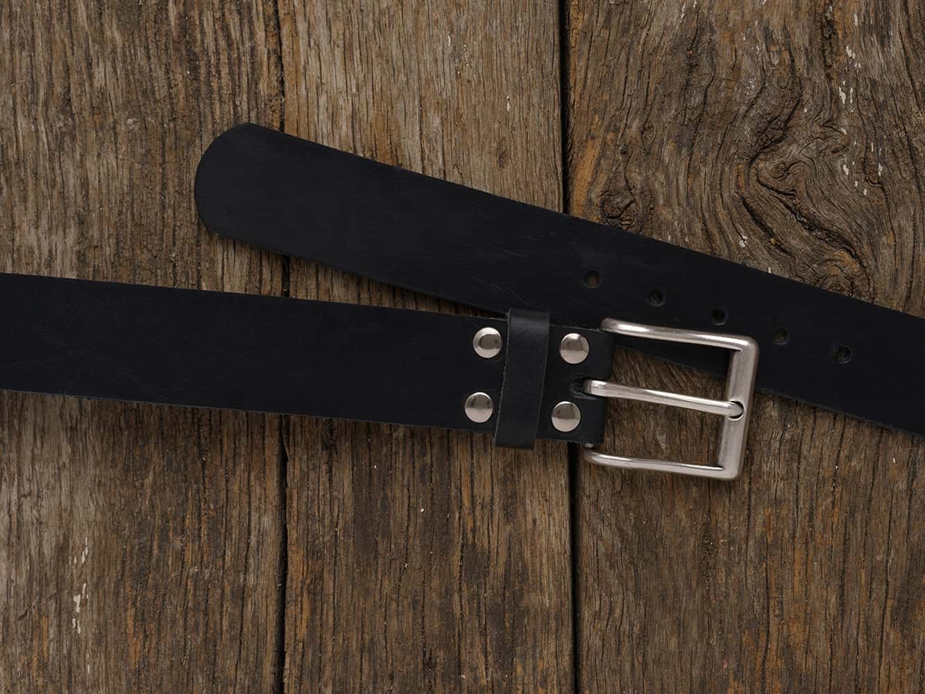 schwarzer Herrengürtel aus Rindsleder mit einer silberfarbenen Schnalle auf einem Holzboden