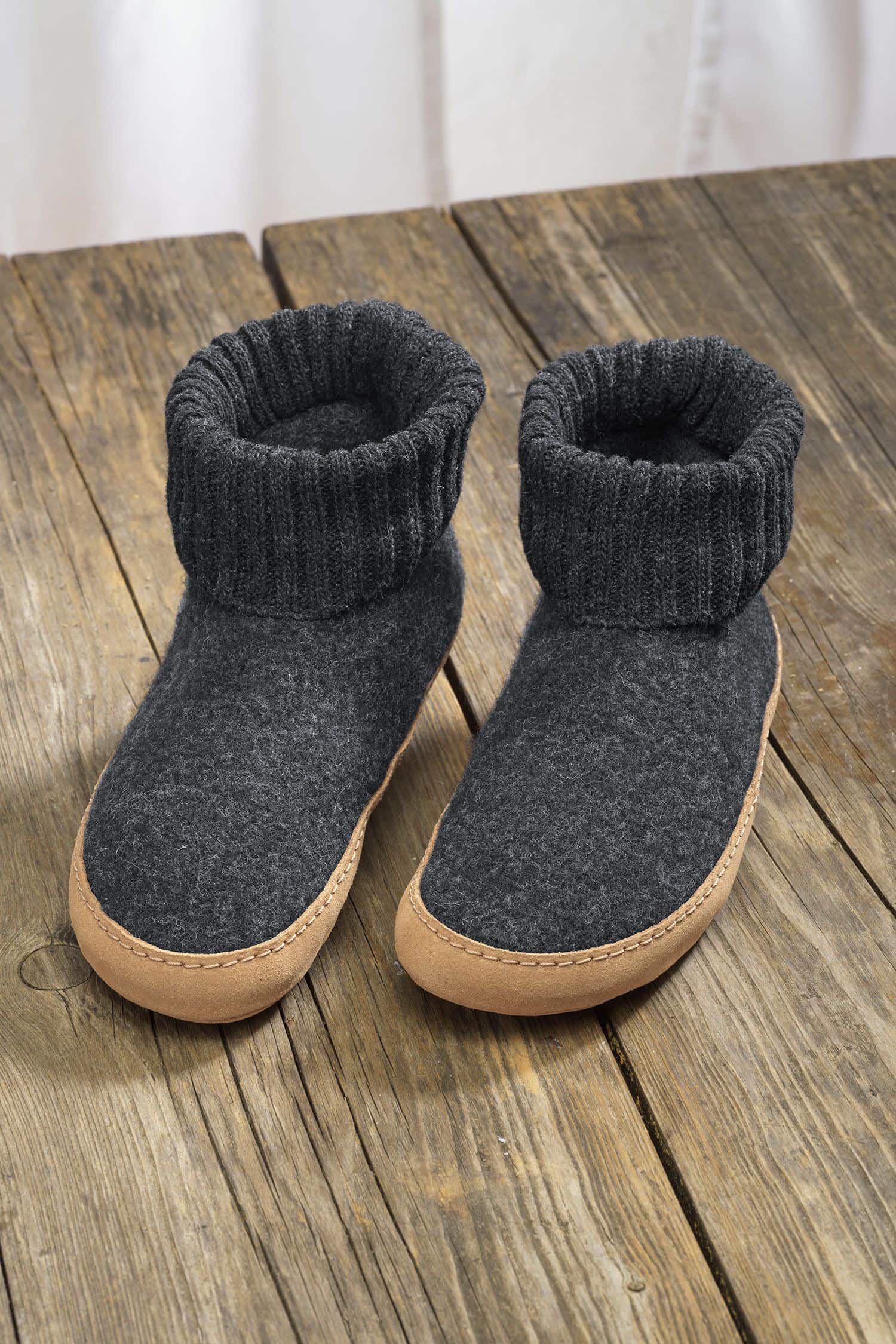 Paar dunkelgraue Finkhof Hüttenschuhe aus bio Wolle (kbT) und einer Sohle aus pflanzlich gegerbtem Rindsleder auf Holzboden
