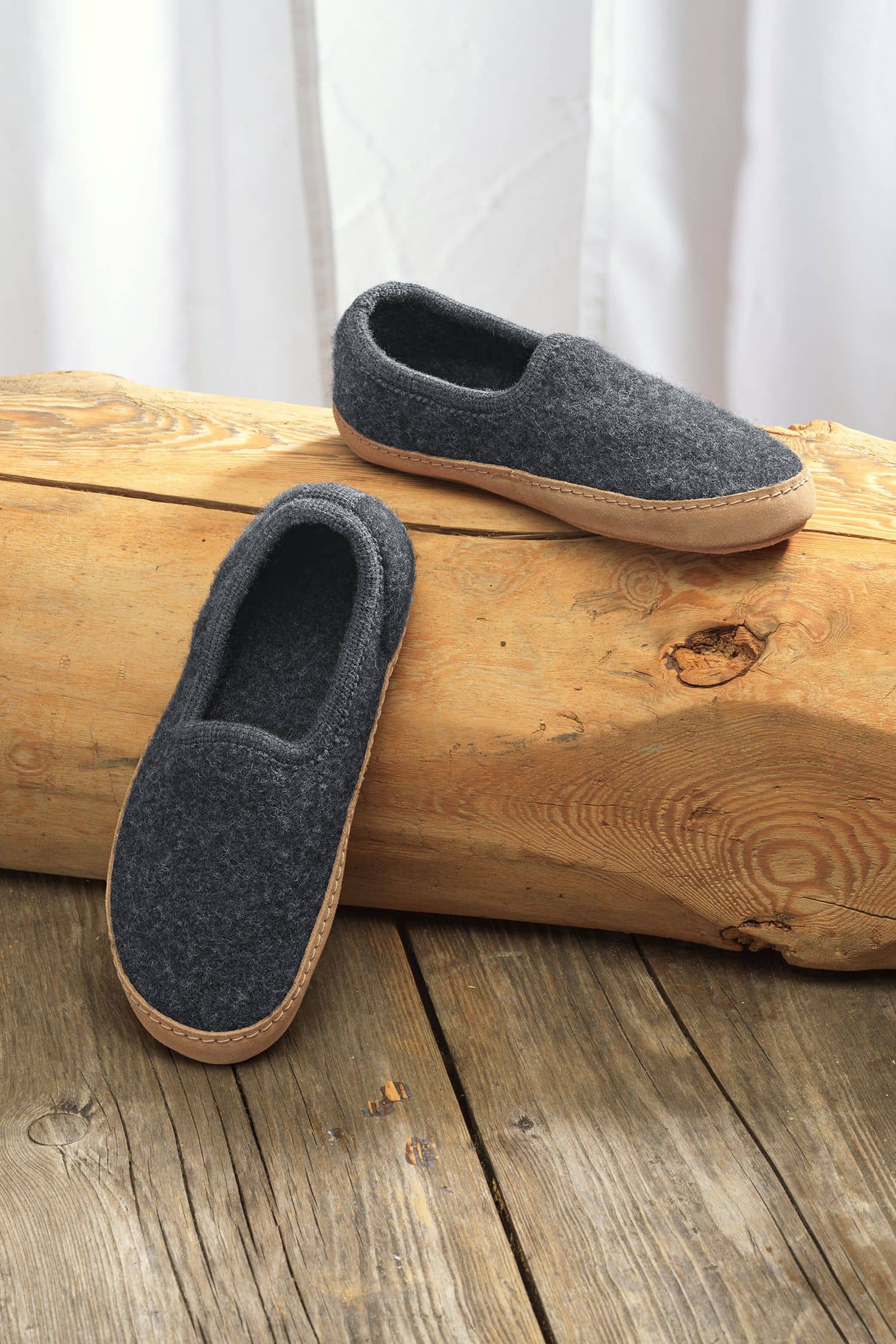 Finkhof-Hausschuhe mit Ledersohle gefärbt Paar dunkelgraue Finkhof Hausschuhe aus bio Wolle (kbT) und einer Sohle aus pflanzlich gegerbtem Rindsleder auf Baumstamm