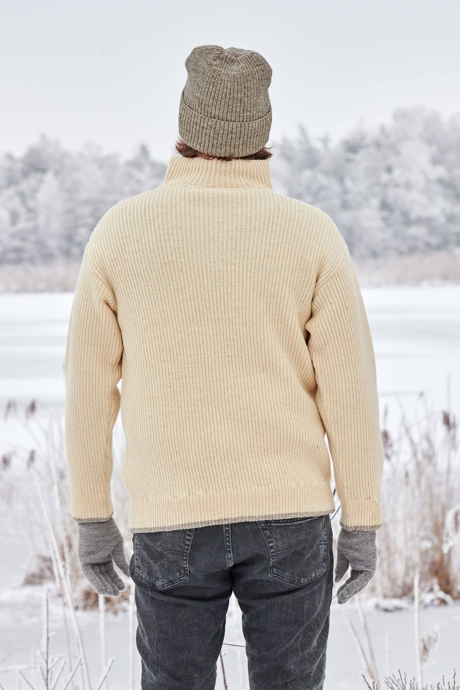Rückansicht von Mann in Schneelandschaft mit naturweißem Finkhof Troyer aus bio Wolle (kbT), grauen Handschuhen und Mütze