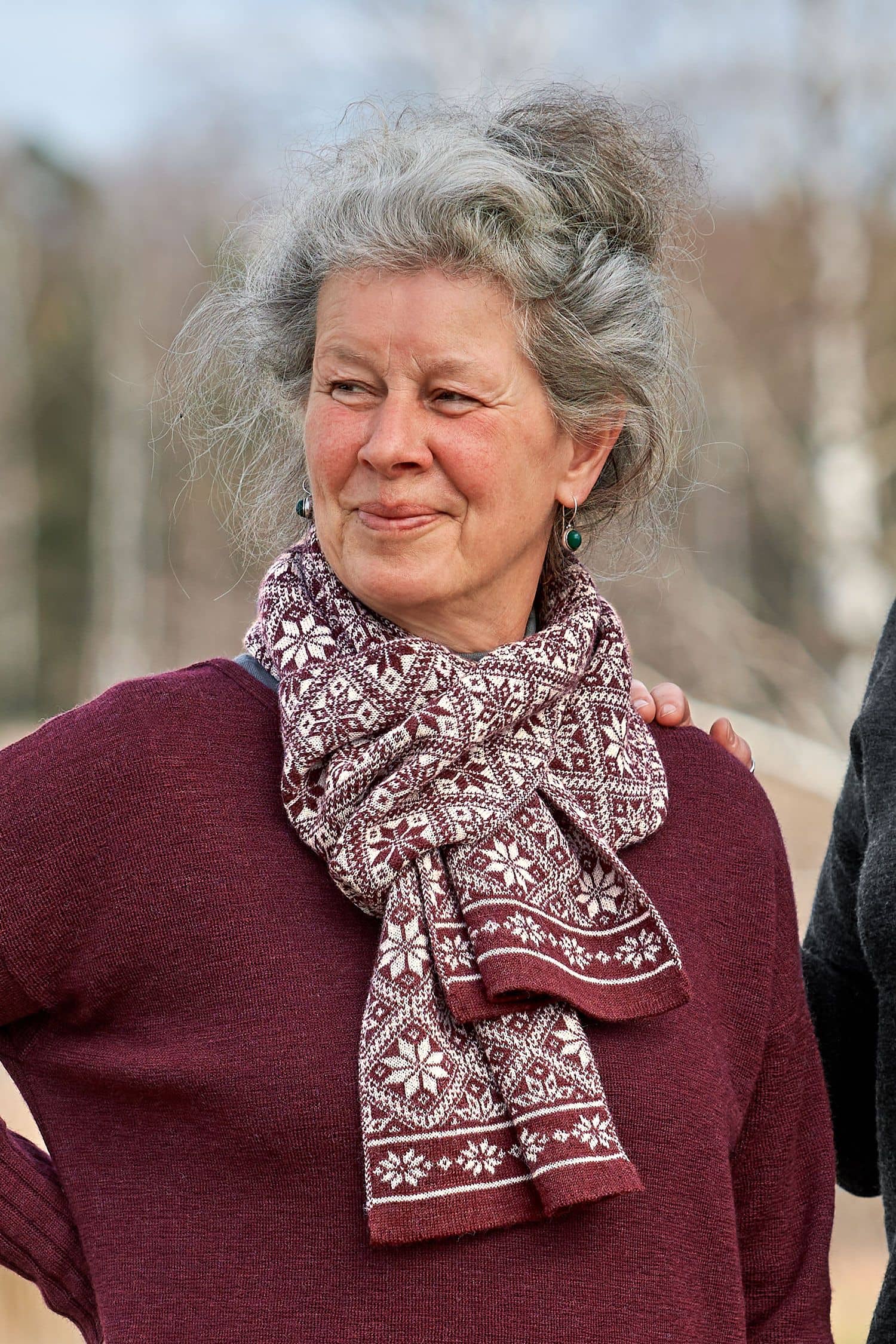 Frau trägt roten Pulli und roten Schal aus bio Wolle (kbT) mit winterlichem Muster