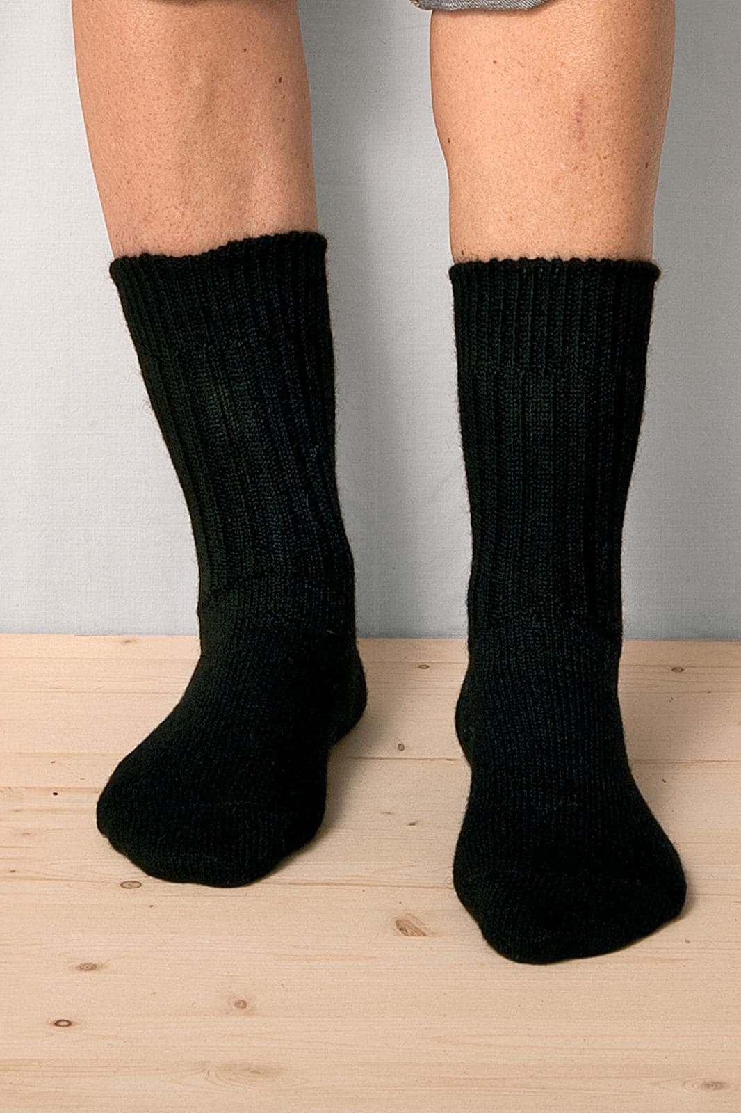 Person steht mit schwarzen Wollsocken aus bio Wolle (kbT) in mittlerer Dicke auf einem Holzboden