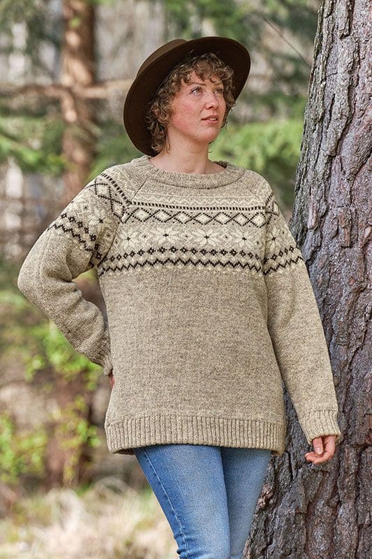 Frau mit Hut steht neben Baum und trägt grauen Finkhof Norwegerpulli aus bio Wolle (kbT)