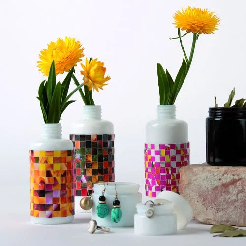 Glasbehälter mit Banderole aus gewebtem Papier mit Blumen, Ohrringen und Glastiegel mit Blättern