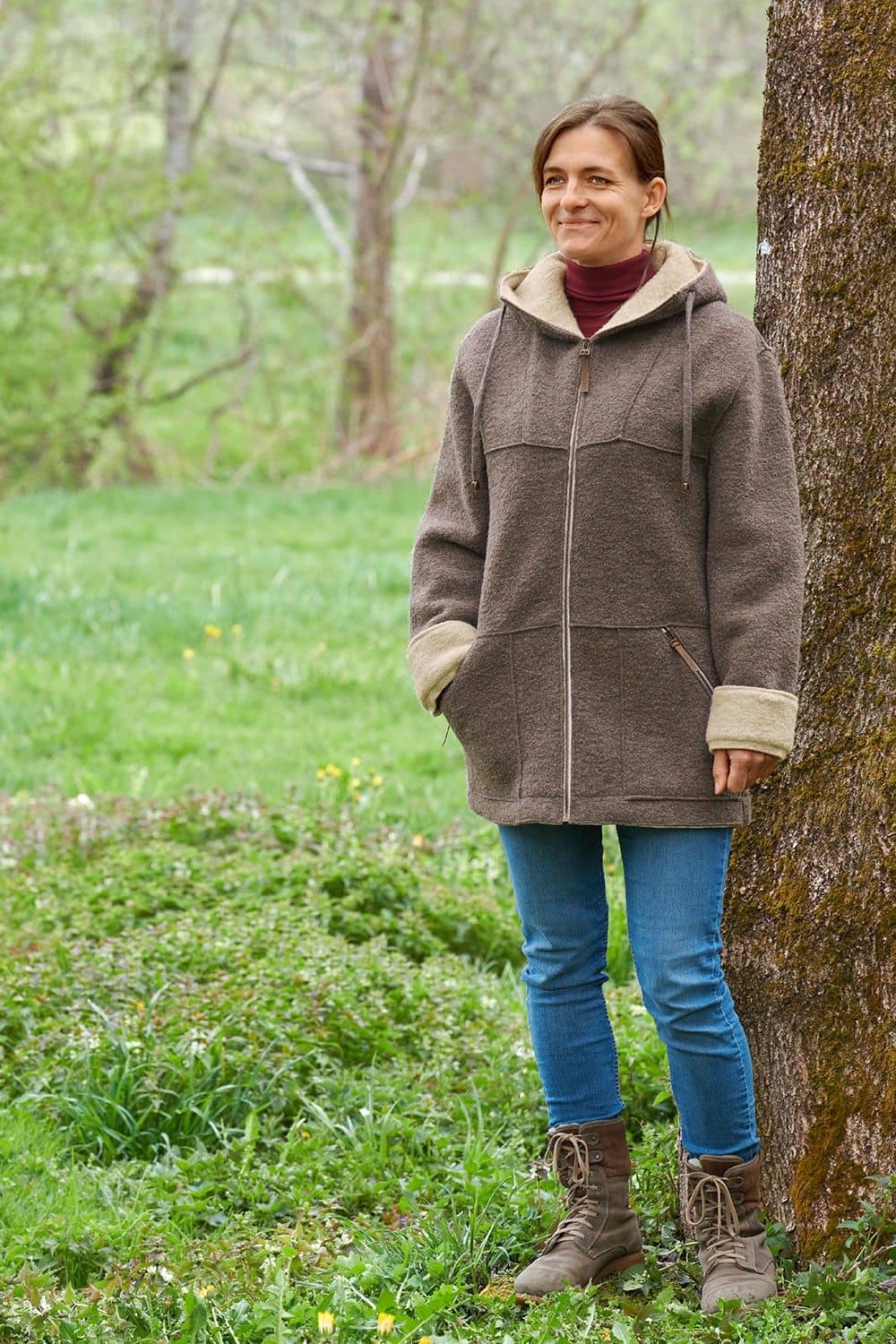 Frau mit Jeans und rotem Shirt trägt walnussbraune Jacke mit Kapuze aus bio Wolle (kbT) vom Finkhof