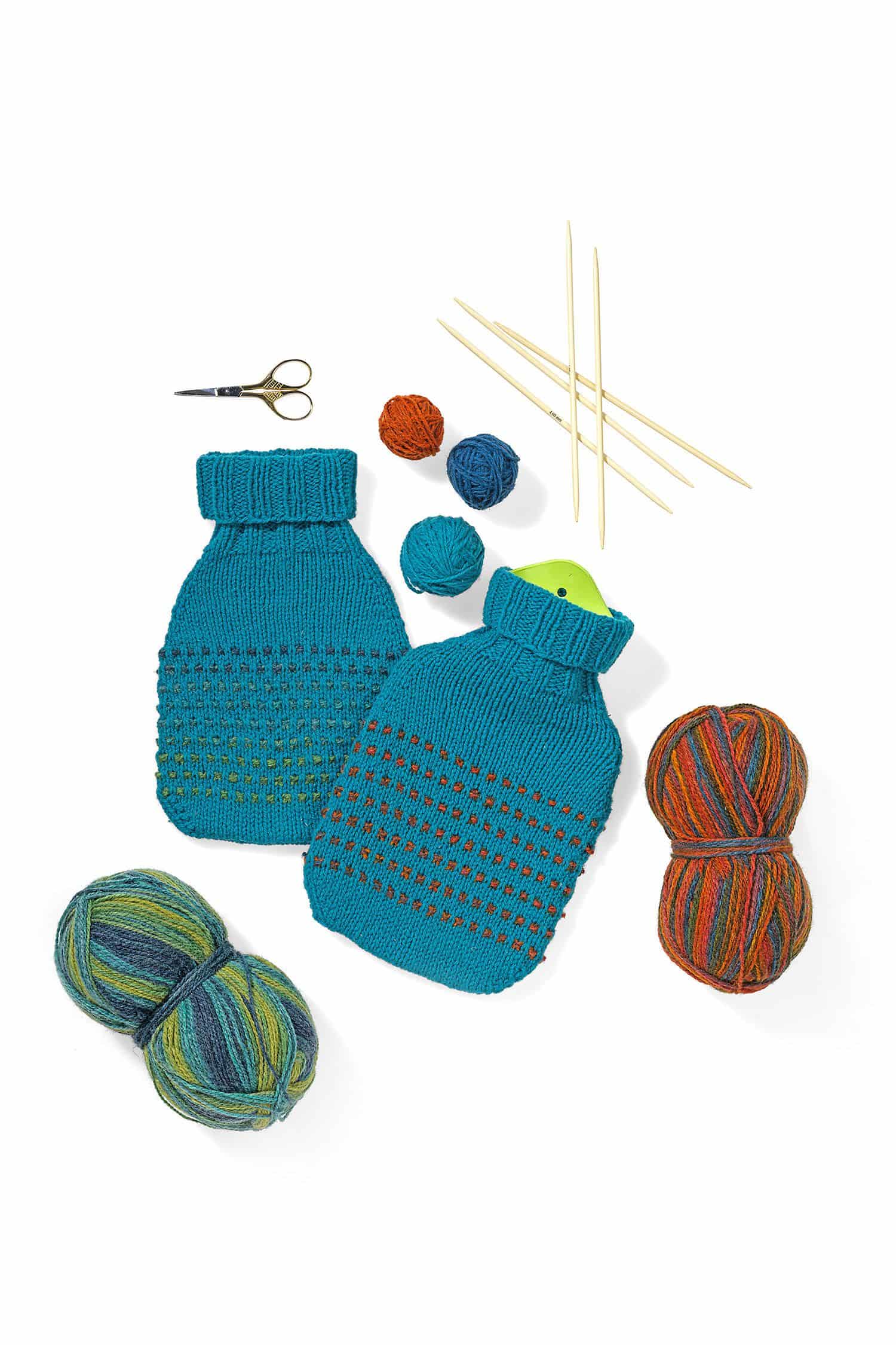 türkis grüner selbstgestrickter Wärmflaschenbezug mit Wollen und Stricknadeln