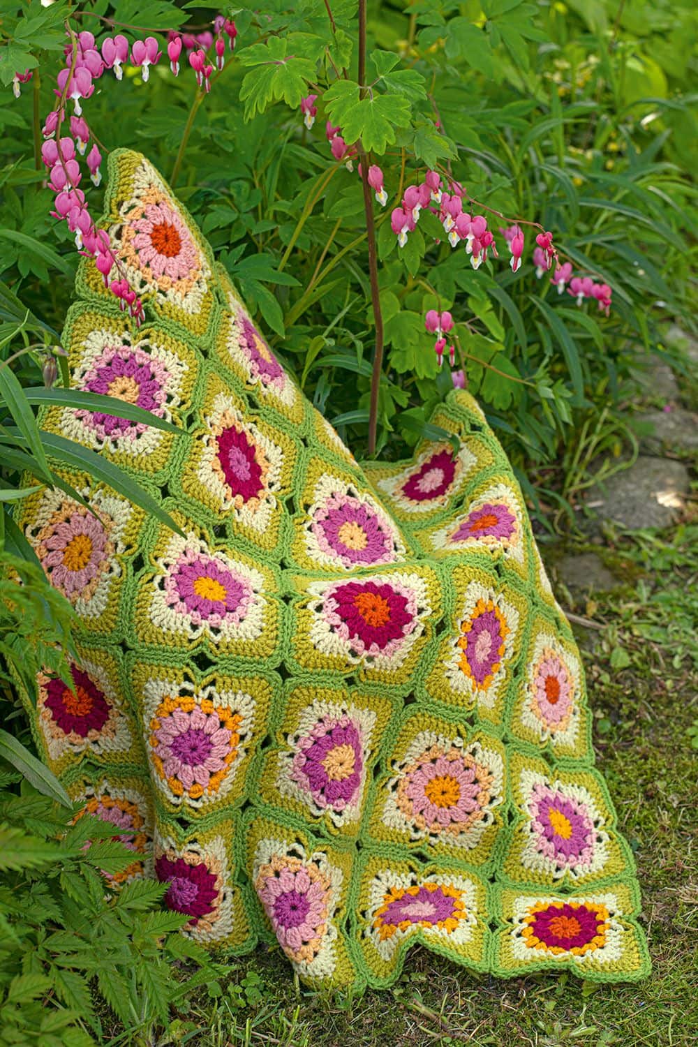 Patchworkdecke in grün und pink aus dem Buch ,,Wunderschöne Häkeldecken" über einem Busch