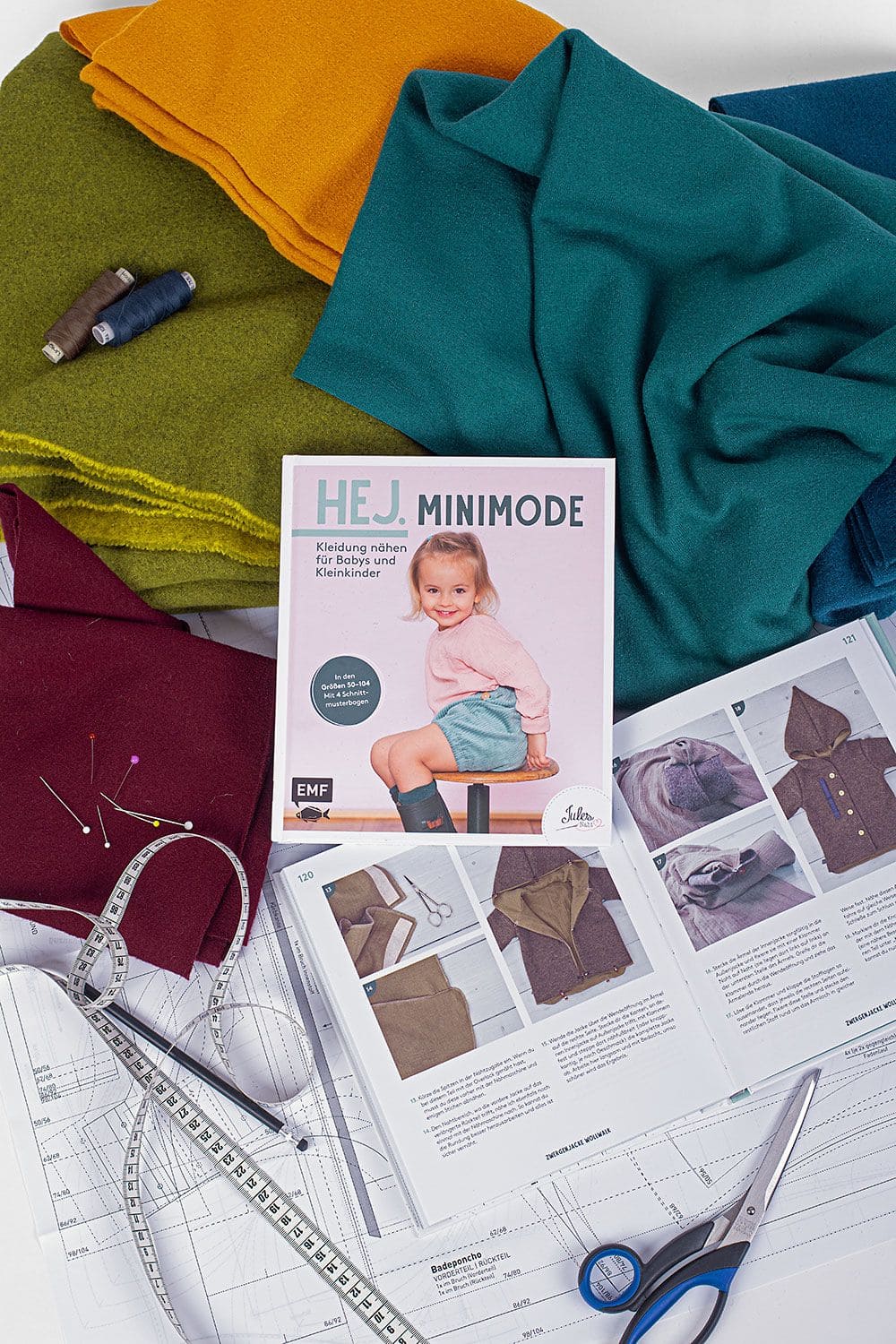 Hej. Minimode Buch ,,HEJ. Minimode" auf verschiedenen Stoffen, aufgeschlagenem Exemplar und Nähutensilien