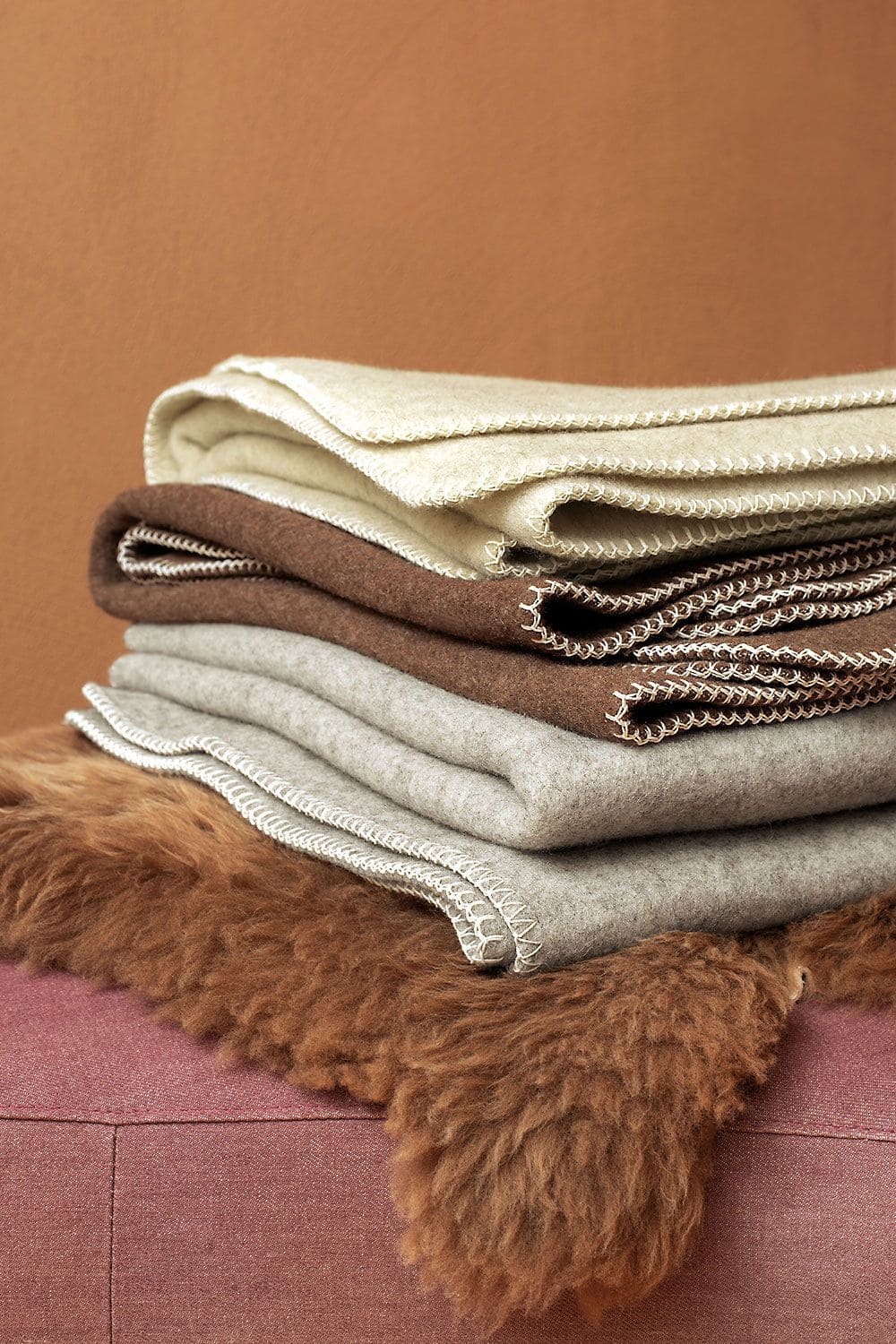 Regionale Wolldecke regionale Wolldecke aus bio Wolle (kbT) ungefärbt in grau, braun und beige über braunem Fell gestapelt