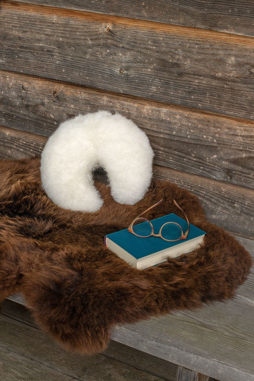 weißes Finkhof Fellhörnchen aus Schaffell und bio Rohwolle (kbT), Buch und Brille liegen auf Bank mit braunem Schaffell